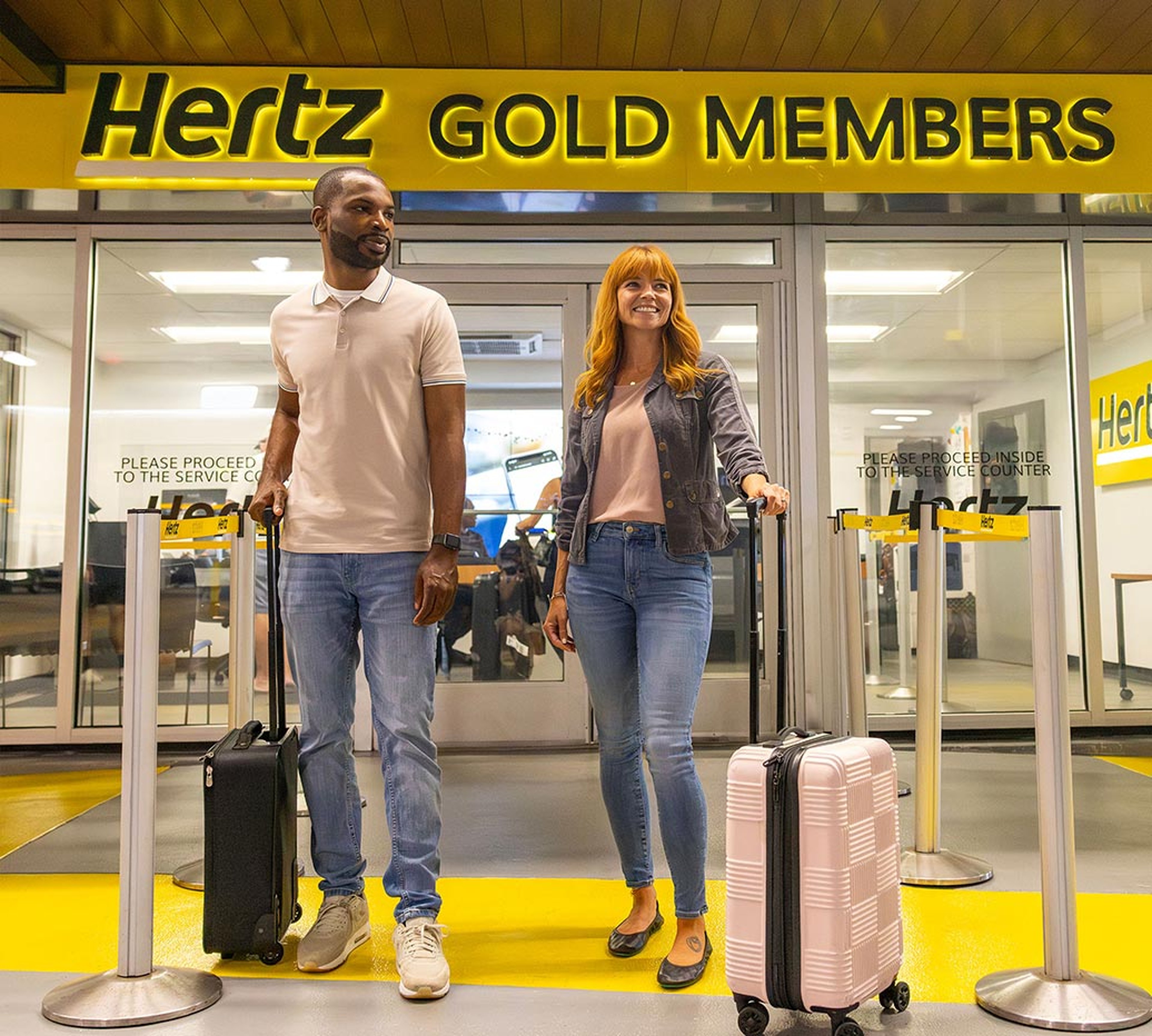 Couple with suitcases standing in front of Hertz Gold Members area