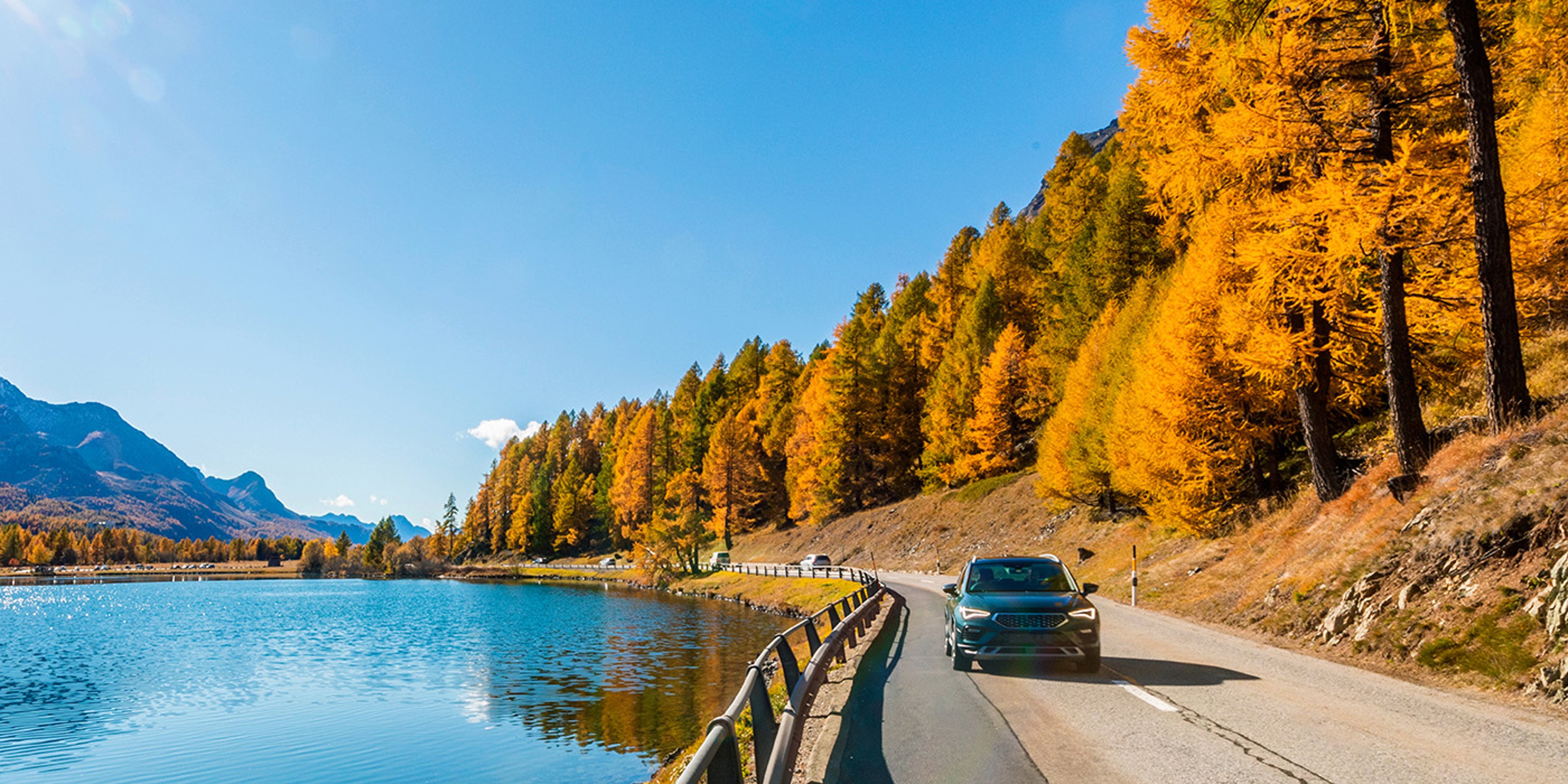 Car driving along scenic highway in fall by a lake