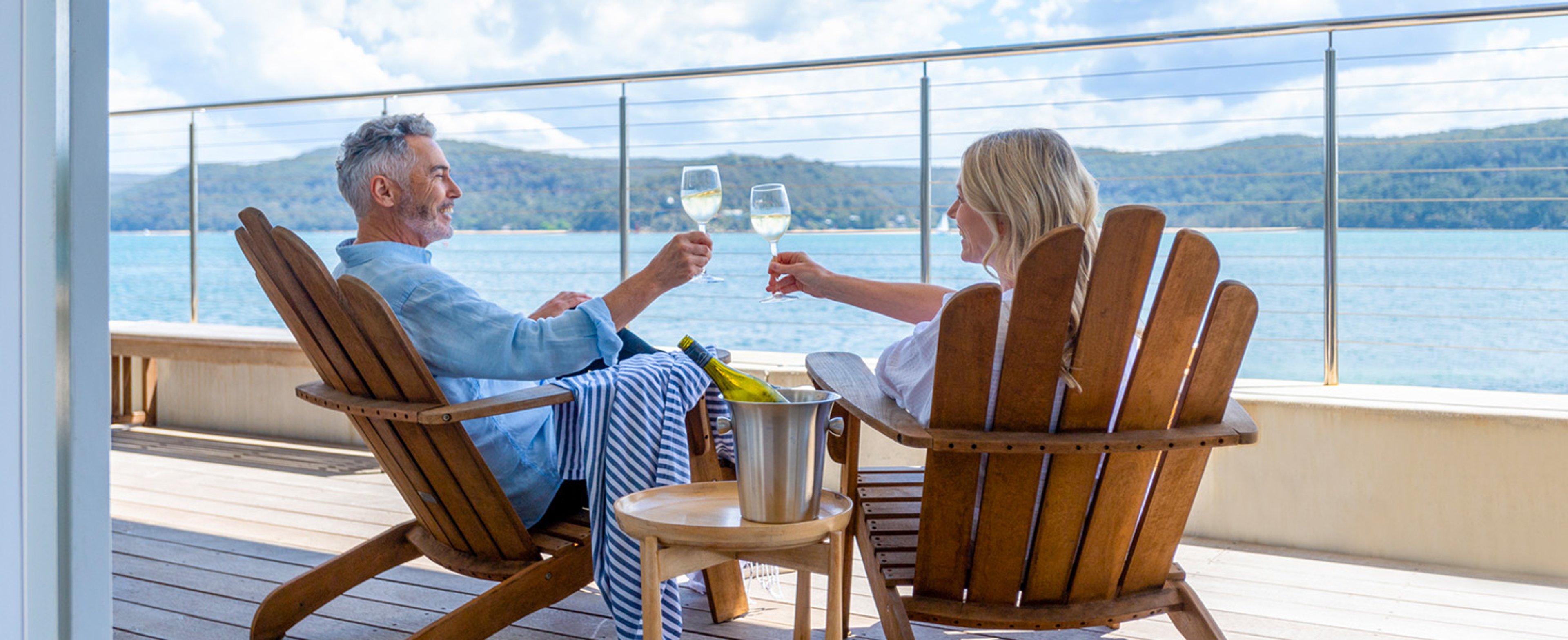 Couple toasting each other while sitting on wooden deck chairs on a cruise ship deck