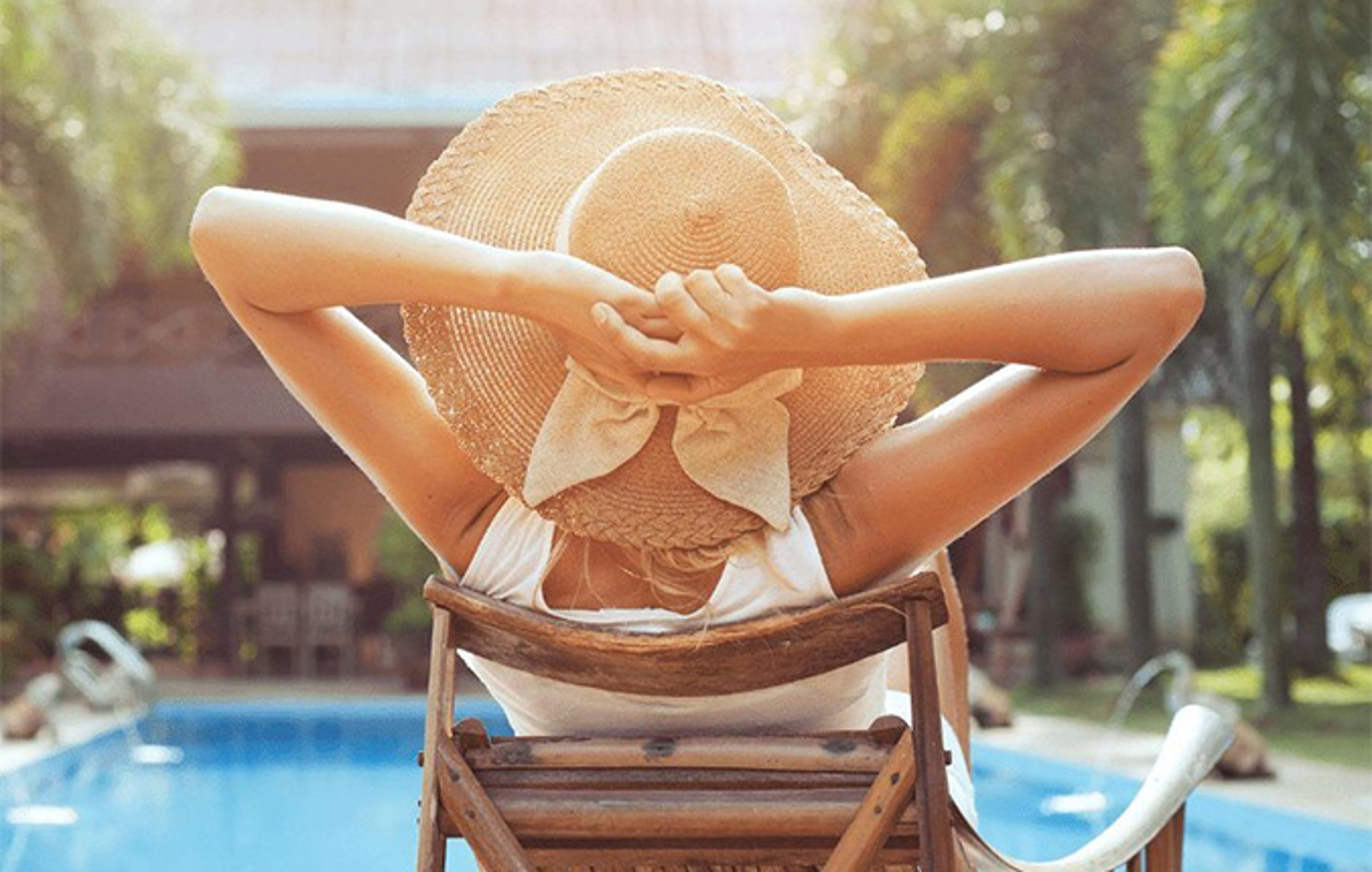 Woman in hat relaxing by pool on vacation