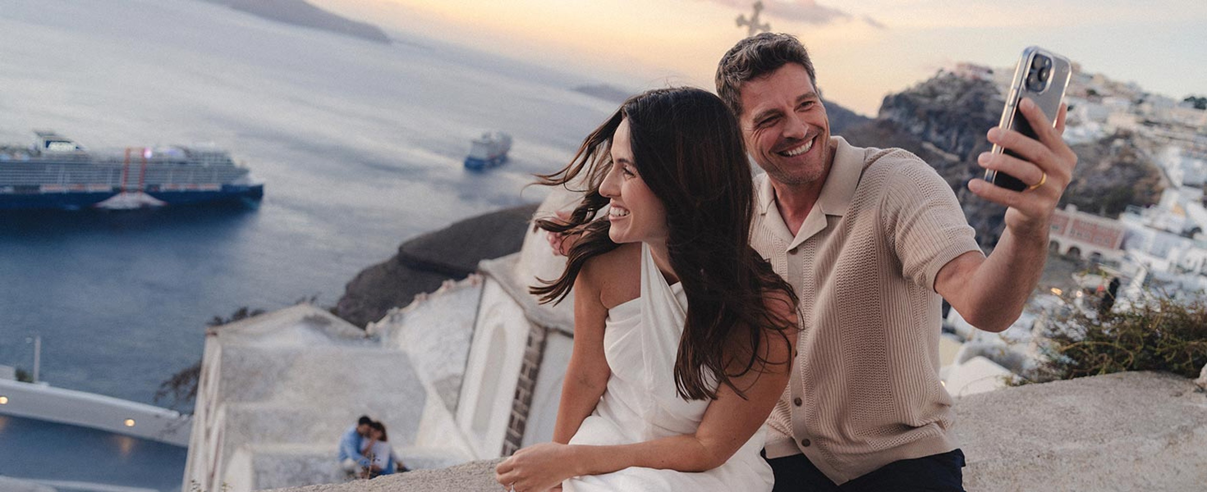 Couple in Santorini with Celebrity ship in background taking picture on phone