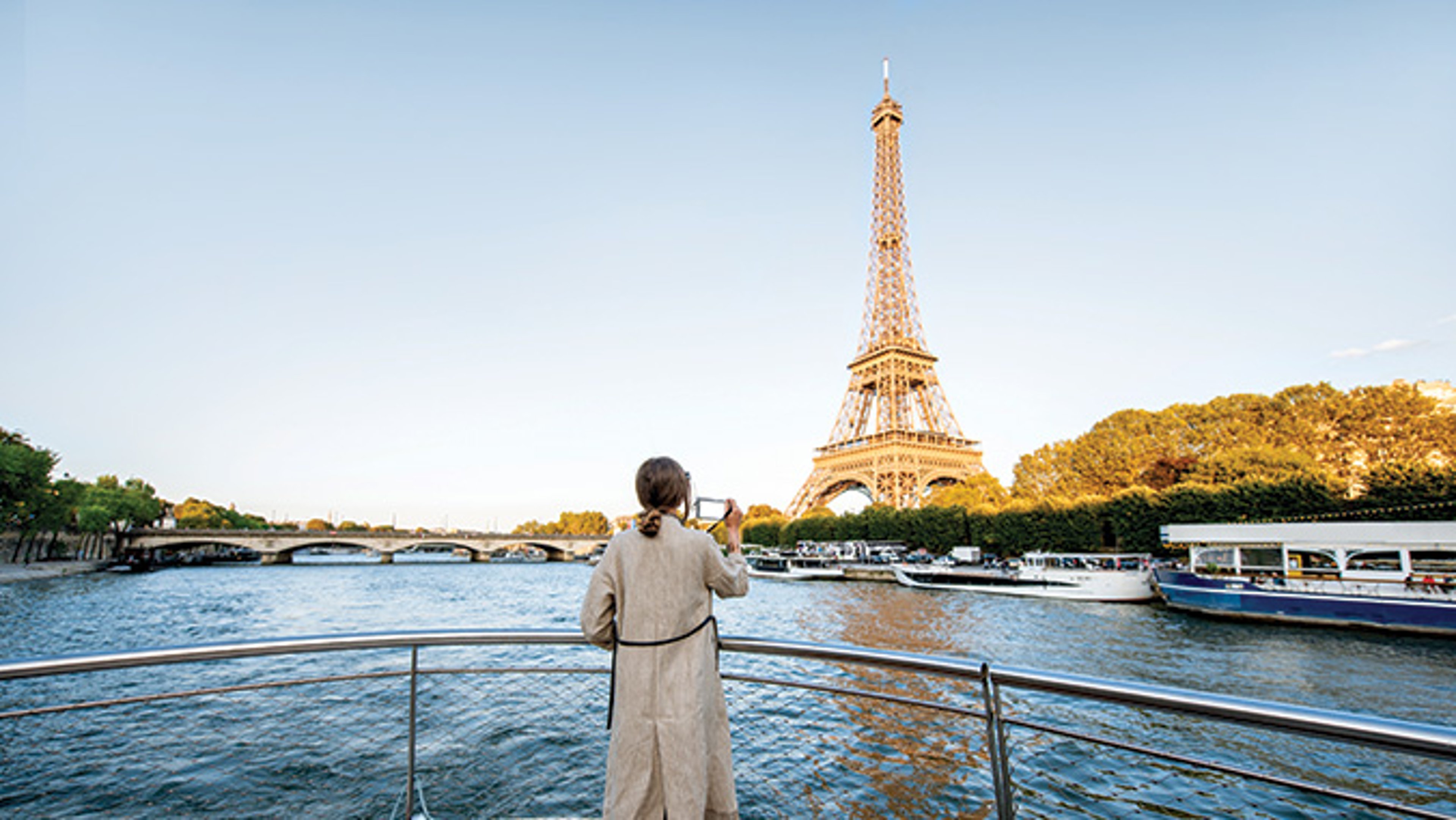 A woman in a white dress gazes at the Eiffel Tower from the deck of a boat.