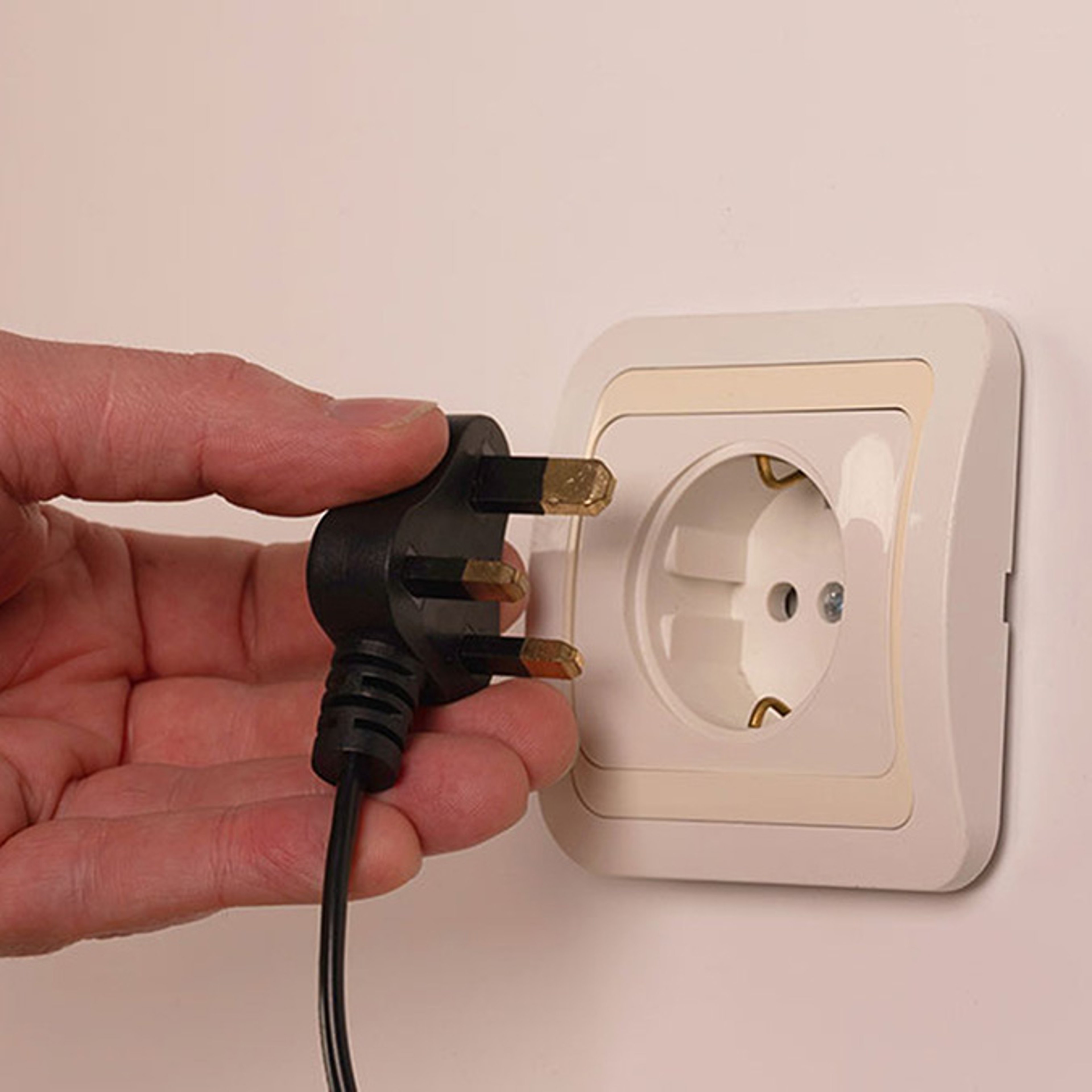 Hand holds a European plug to a wall outlet.