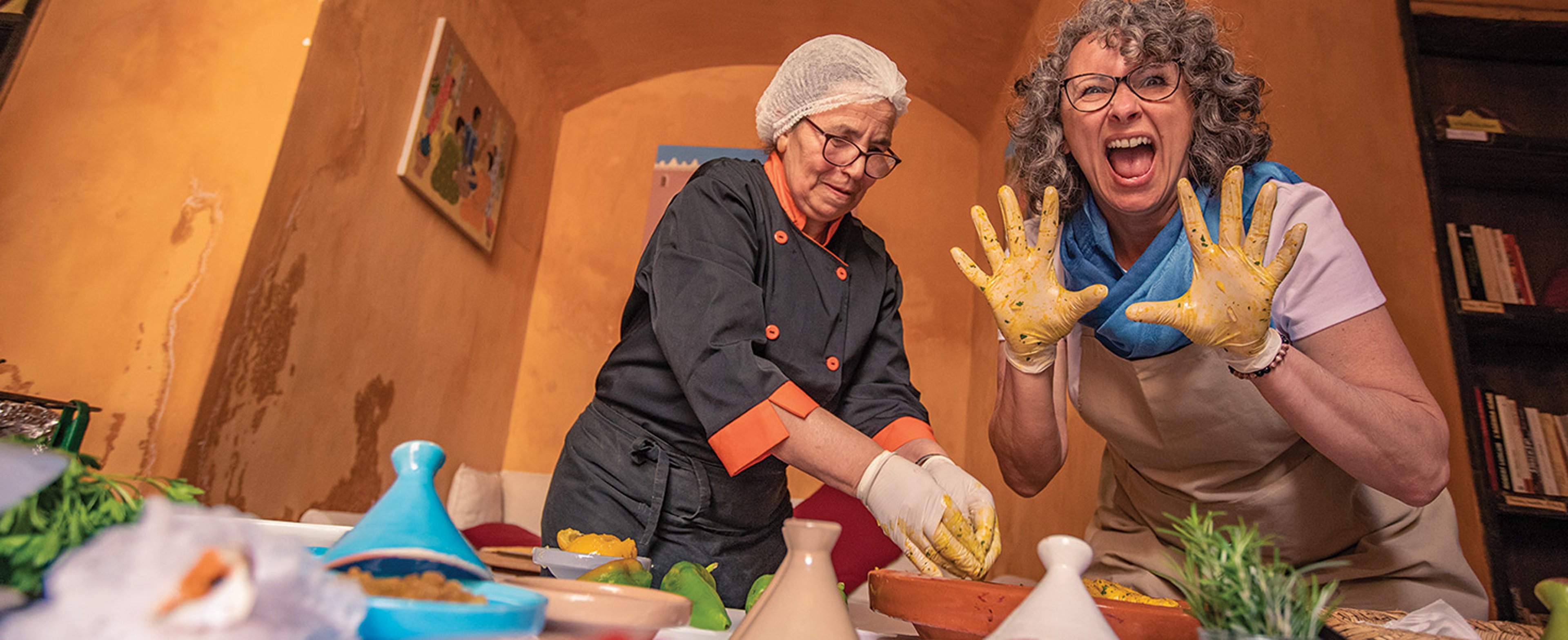 Woman holding up clay covered hands at a ceramics class in Marrakech, Morocco while standing next to the woman instructor