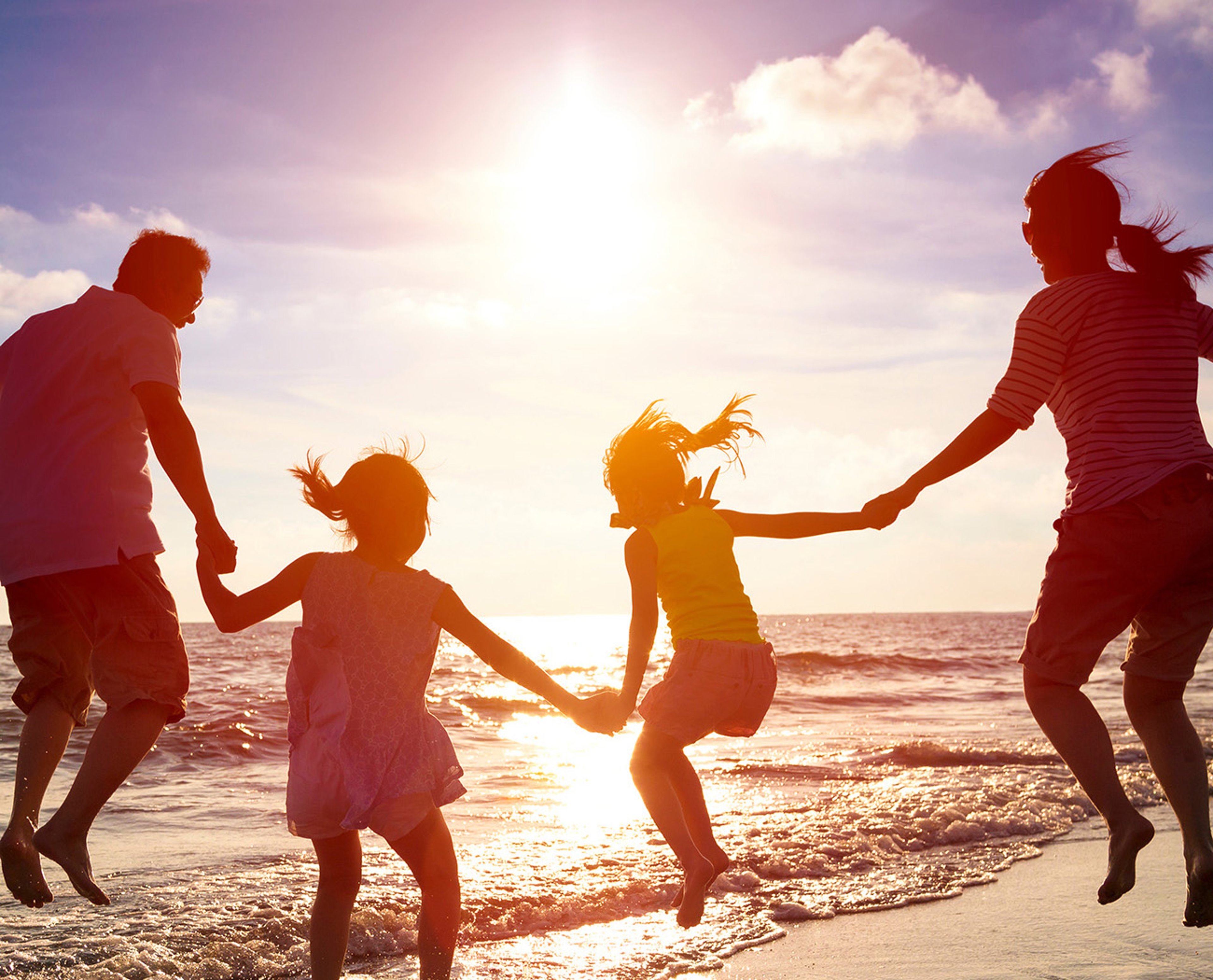 Family holding hands and jumping on sunlit beach while on vacation