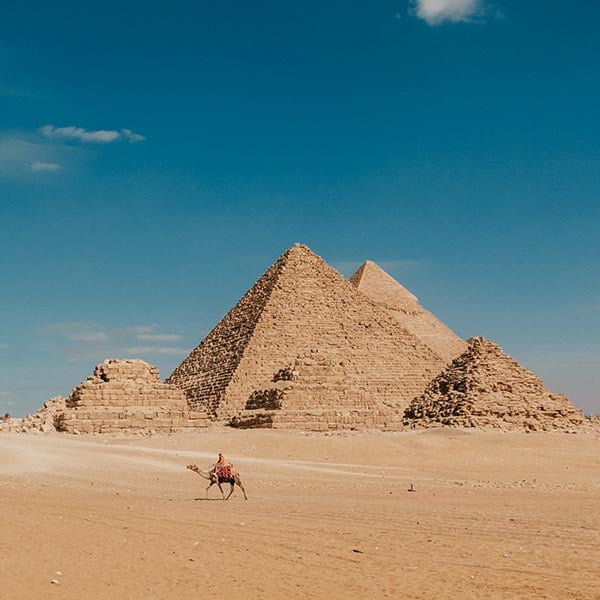 Giza pyramid complex, located on the outskirts of Cairo, Egypt with a person riding a camel in the forefront.