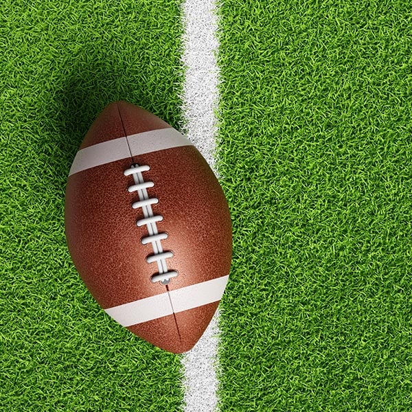 Football placed on a painted yard line on a green football field, ready for play.