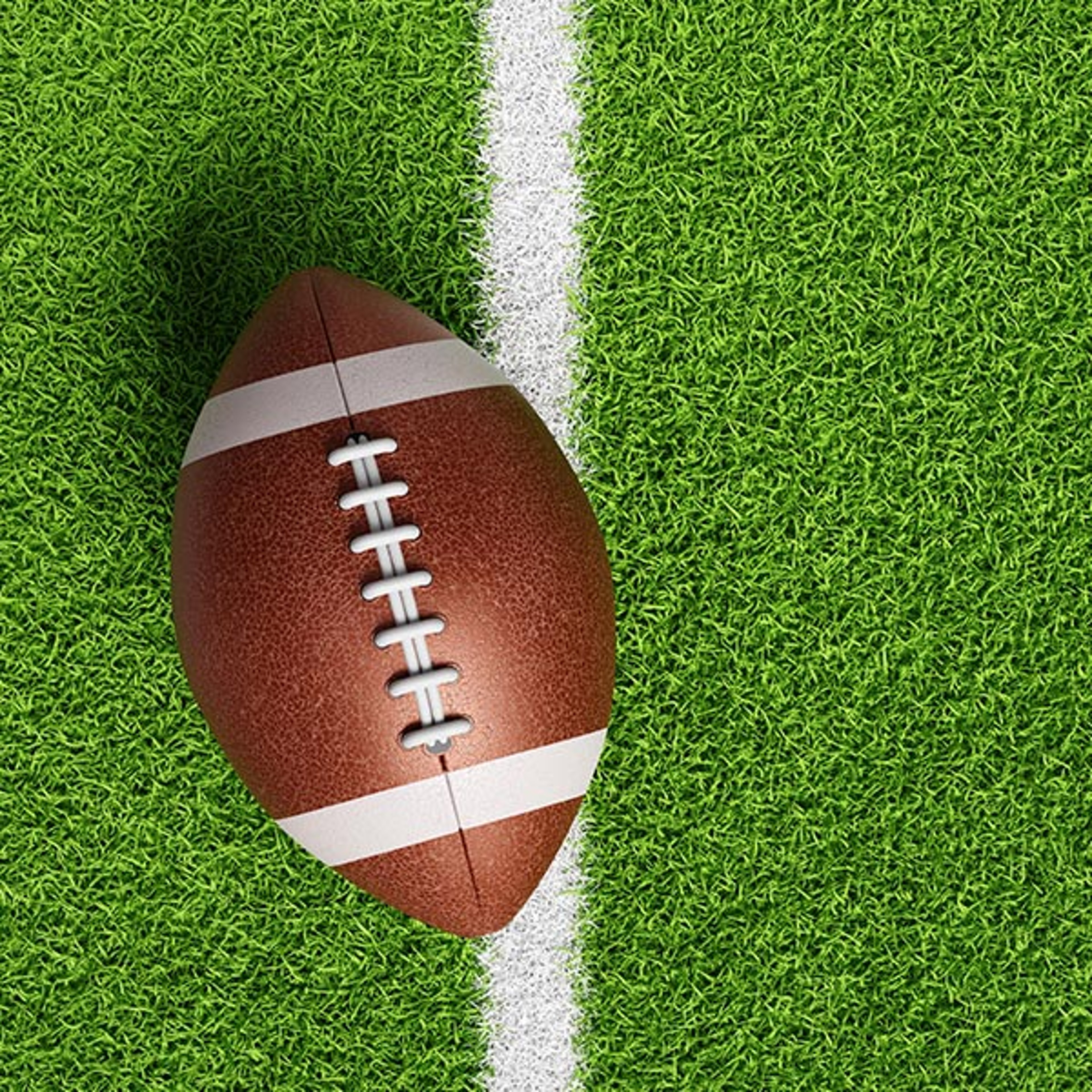 Football placed on a painted yard line on a green football field, ready for play.
