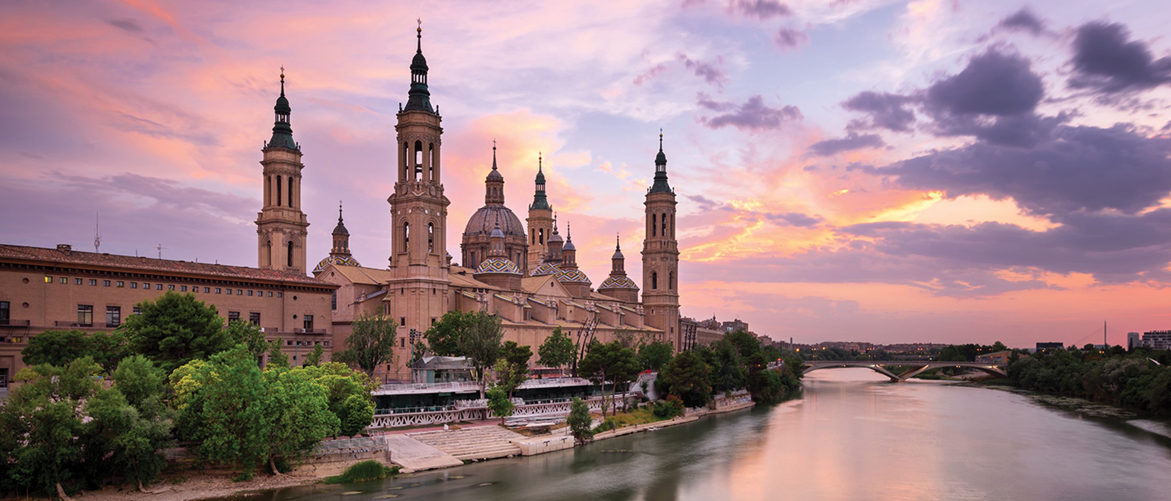 The image shows the Cathedral-Basilica of Our Lady of the Pillar sitting along the Ebro River in Zaragoza, Spain.