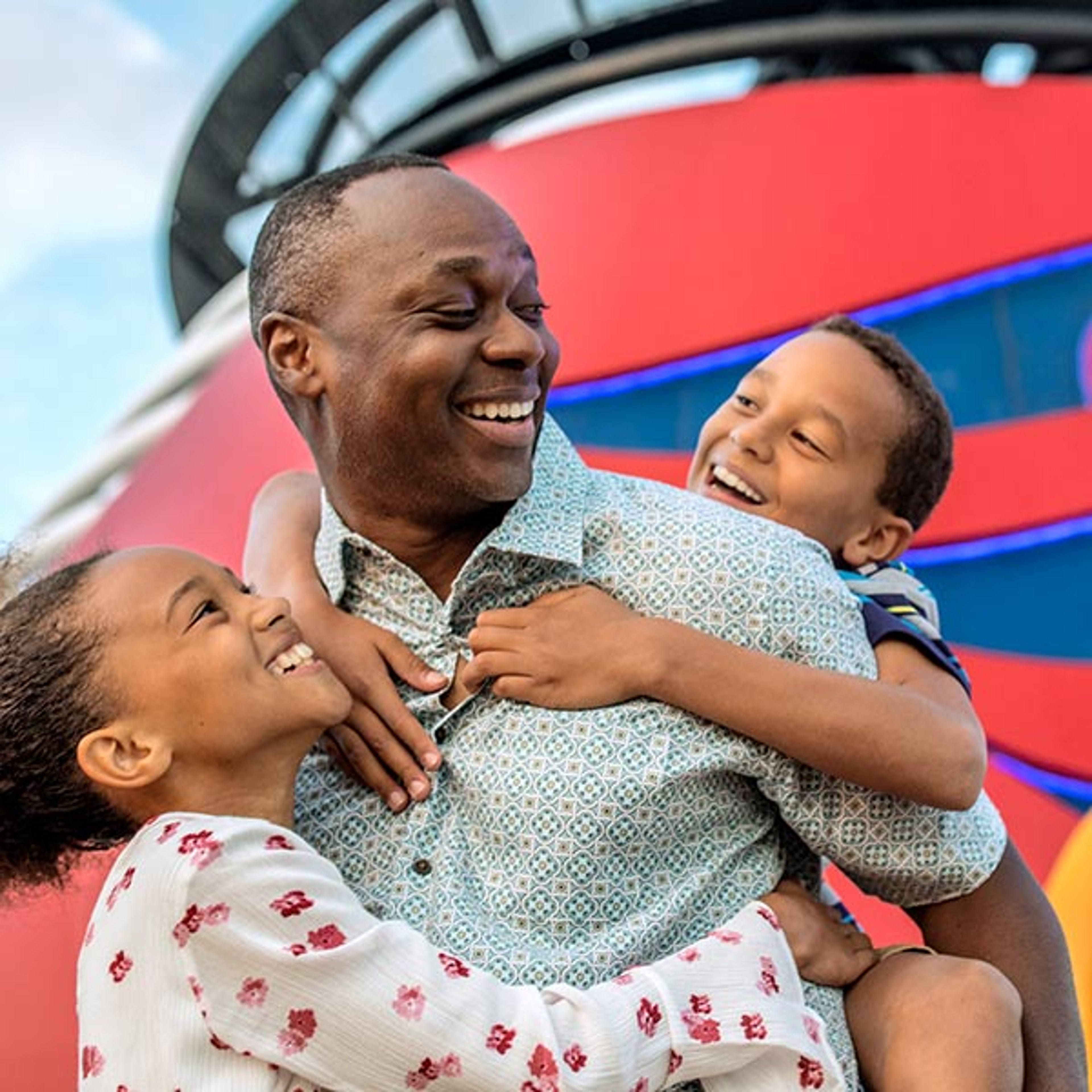 A dad being hugged by his two kids in front of a Disney Cruise Line smokestack