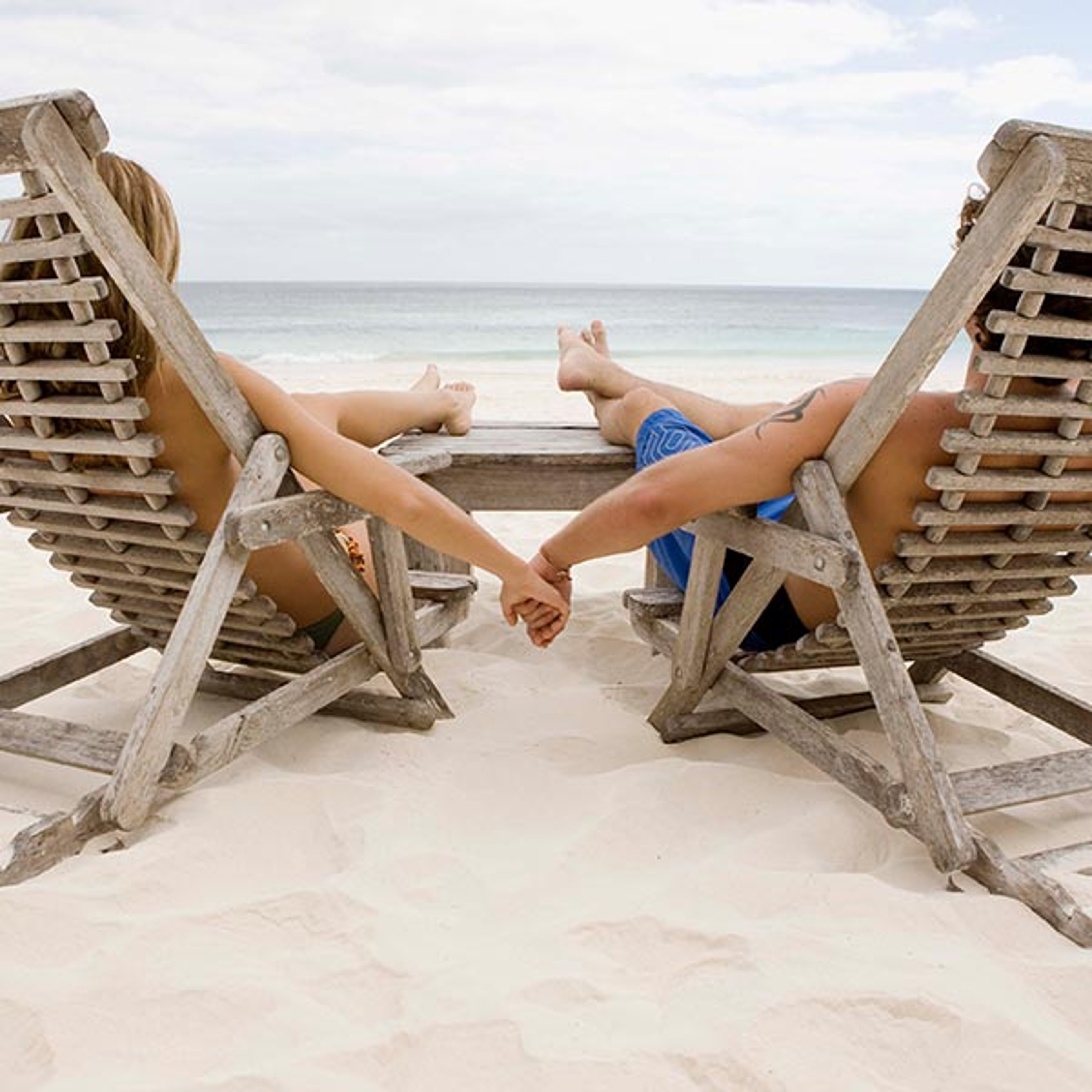 Couple holding hands while sitting in lounge chairs at the beach