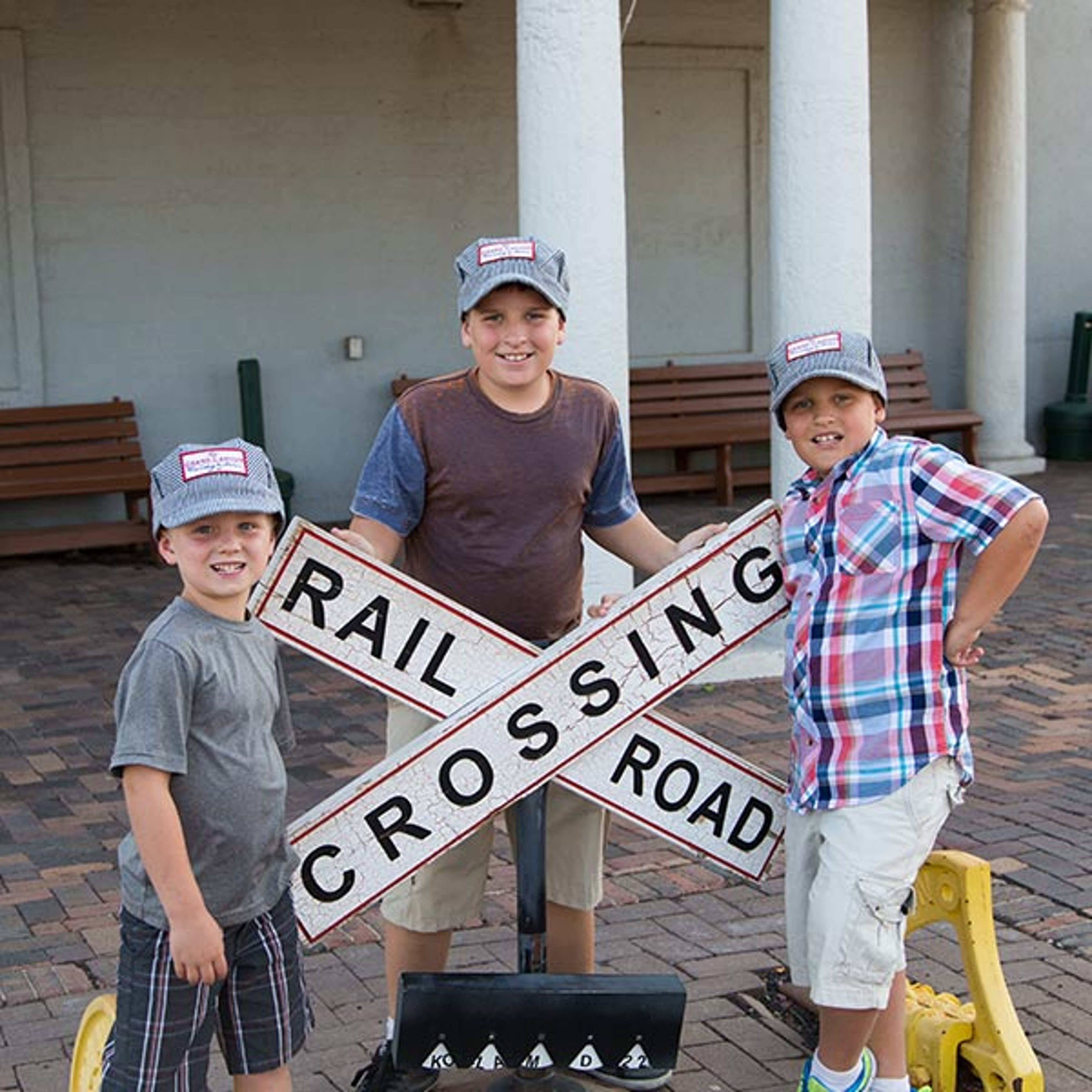 Three boys posing with railroad crossing sign