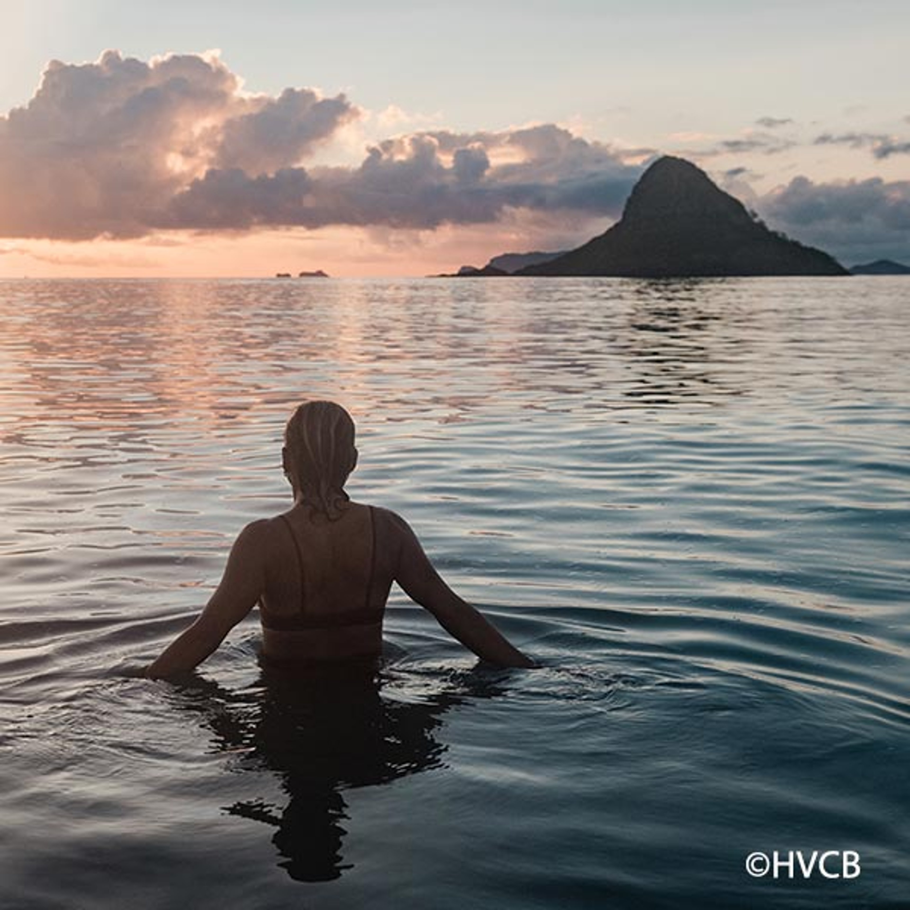 Woman standing in the ocean waters admiring the sunset over Hawaii
