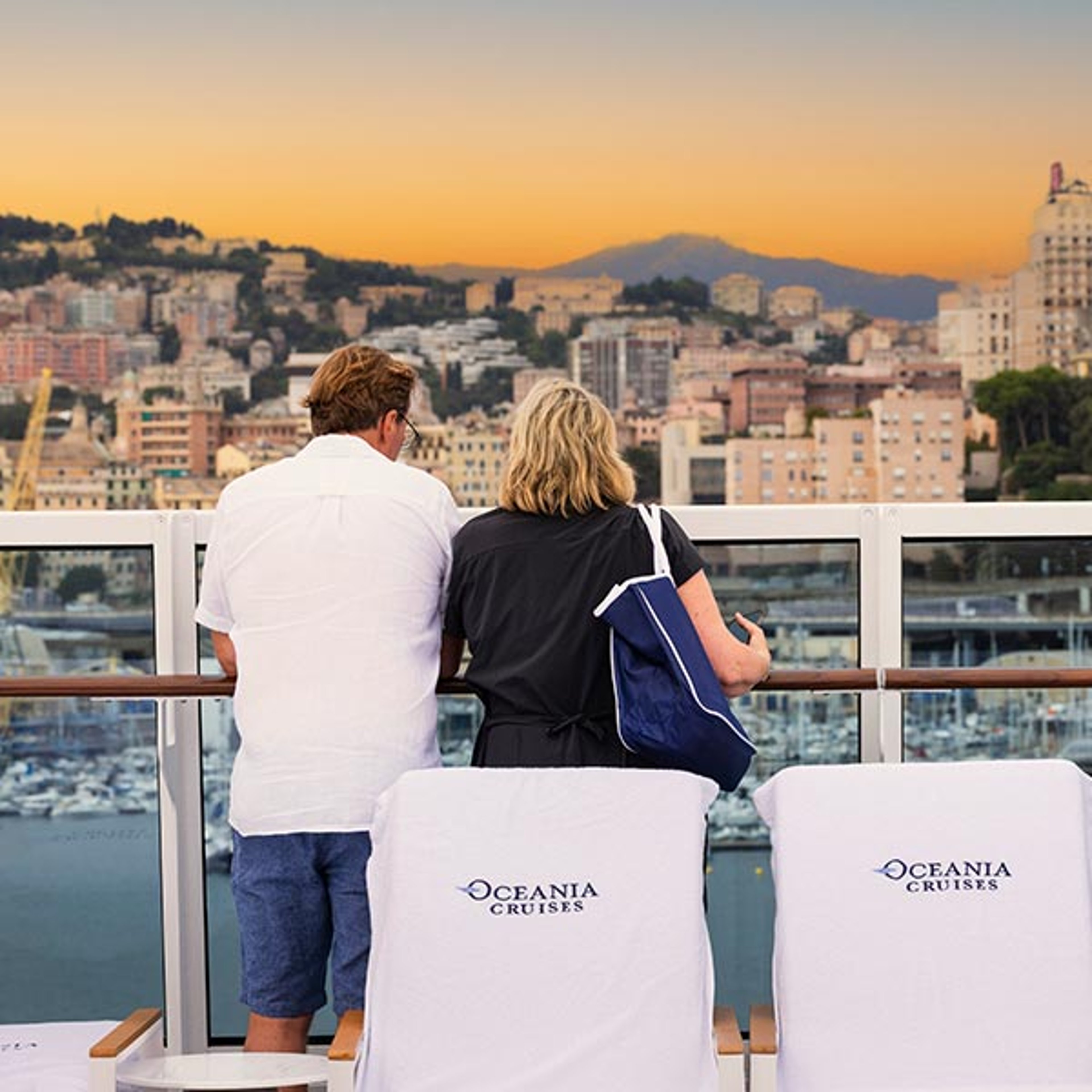 A couple aboard an Oceania cruise watching the sail away from the dock