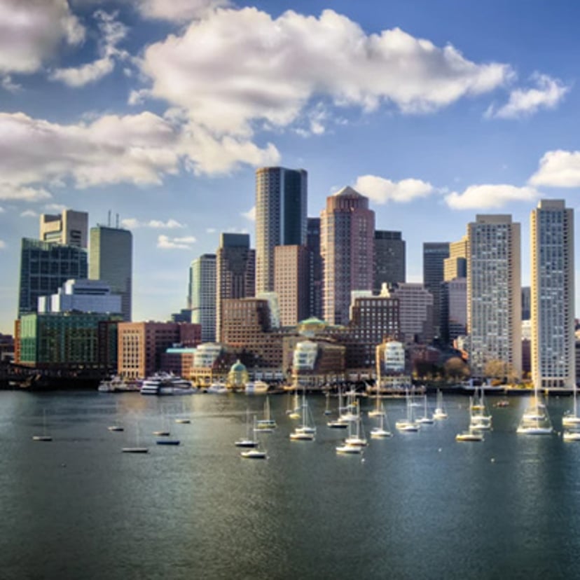 Boston skyline overlooking the harbor with sailboats in the foreground.