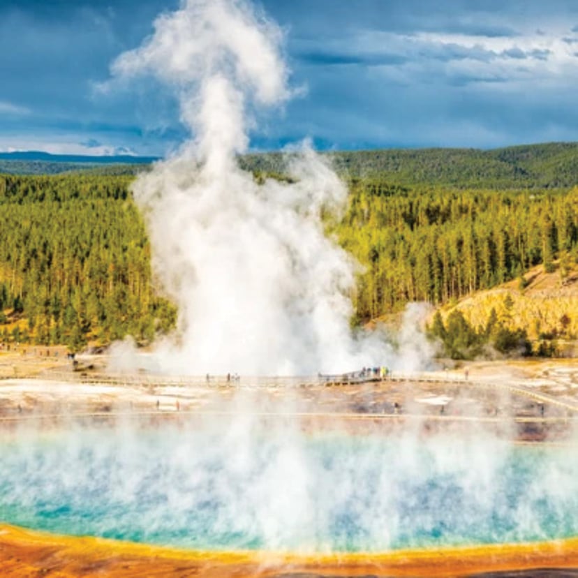 Geyser erupting beside a colorful geothermal pool in Yellowstone National Park.