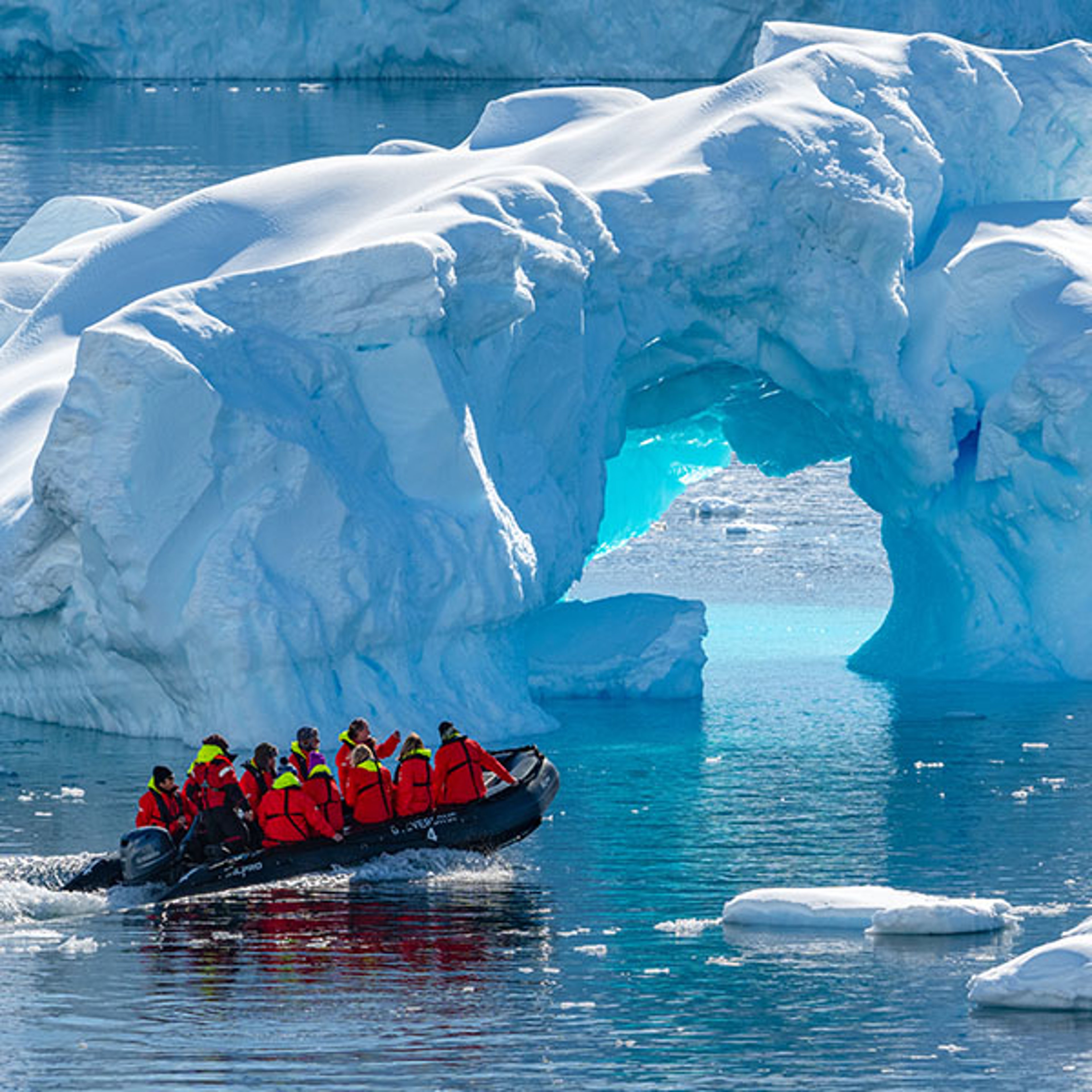Tourists in an inflatable boat approaching a large glacier arch during an expedition cruise.