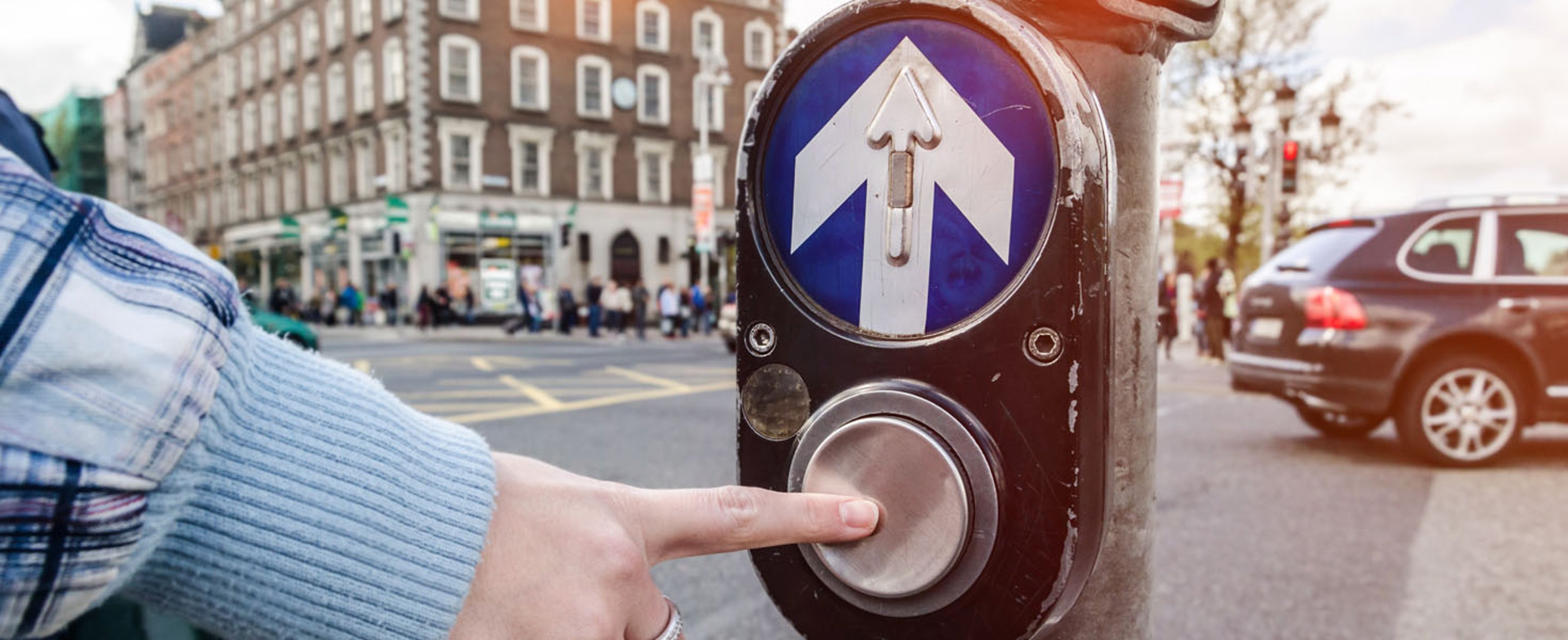Person pushing a cross walk button at corner of busy intersection in Ireland