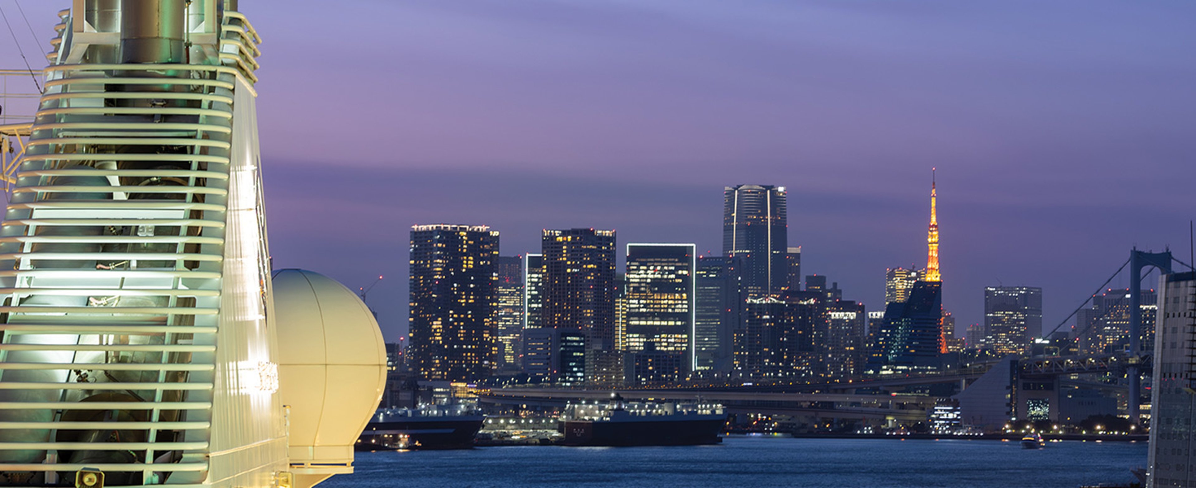 Silversea ship docked in Tokyo, showing the Yokohama skyline at twilight, featuring the distinctive curved architecture of the InterContinental Yokohama Grand hotel