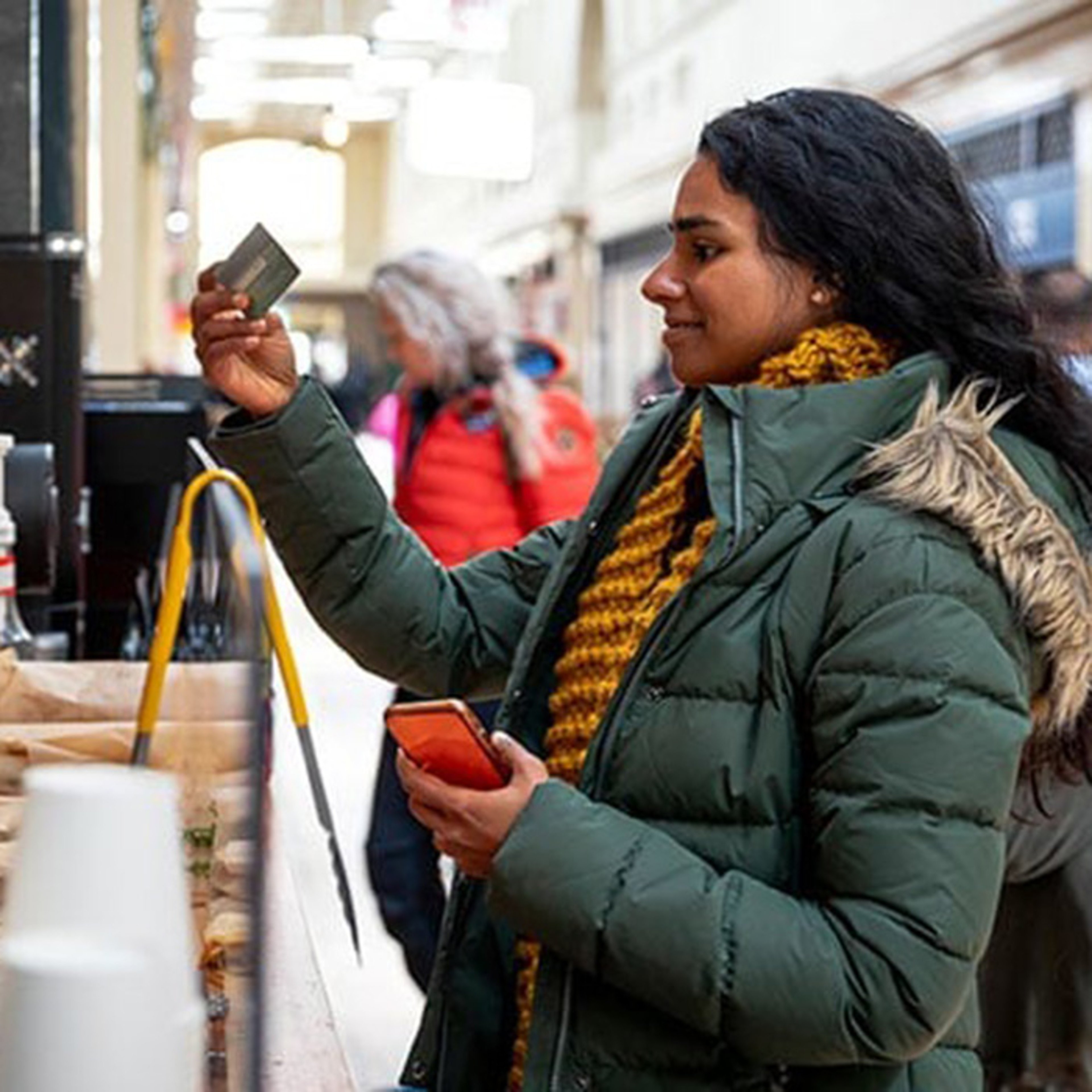 Young woman in winter coat holding credit card up to pay tip while traveling