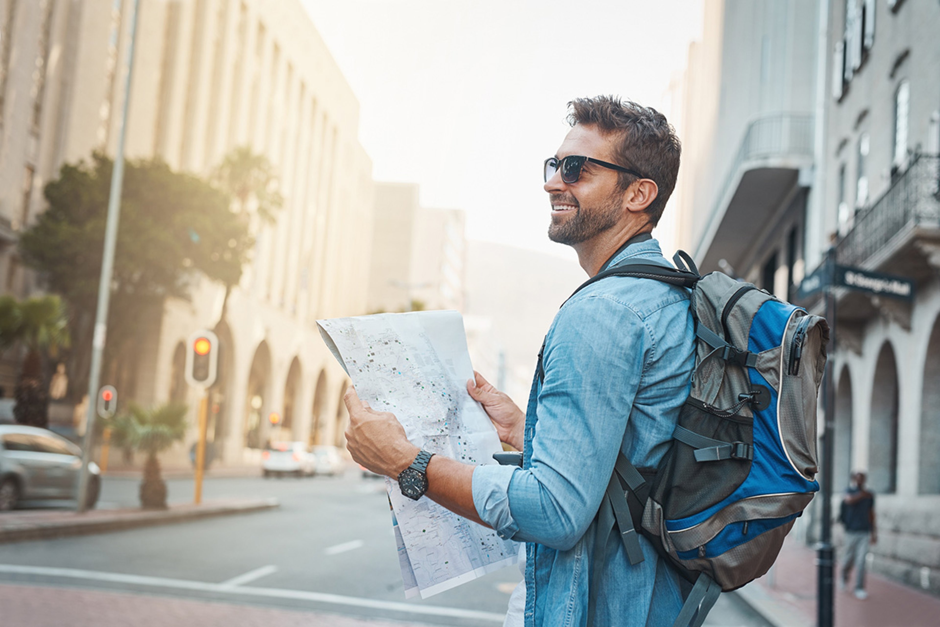 Smiling man with sunglasses and backpack holding map on bustling city street