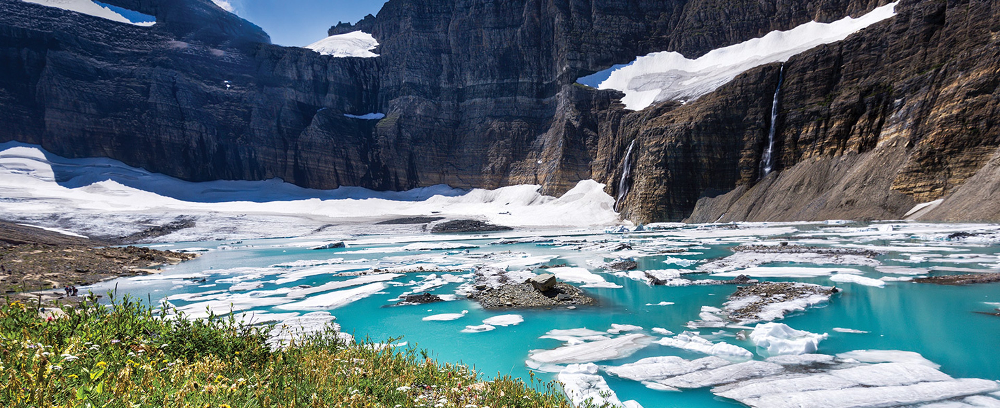 Turquoise waters dotted with pieces of ice surrounded by mountains in Glacier National Park