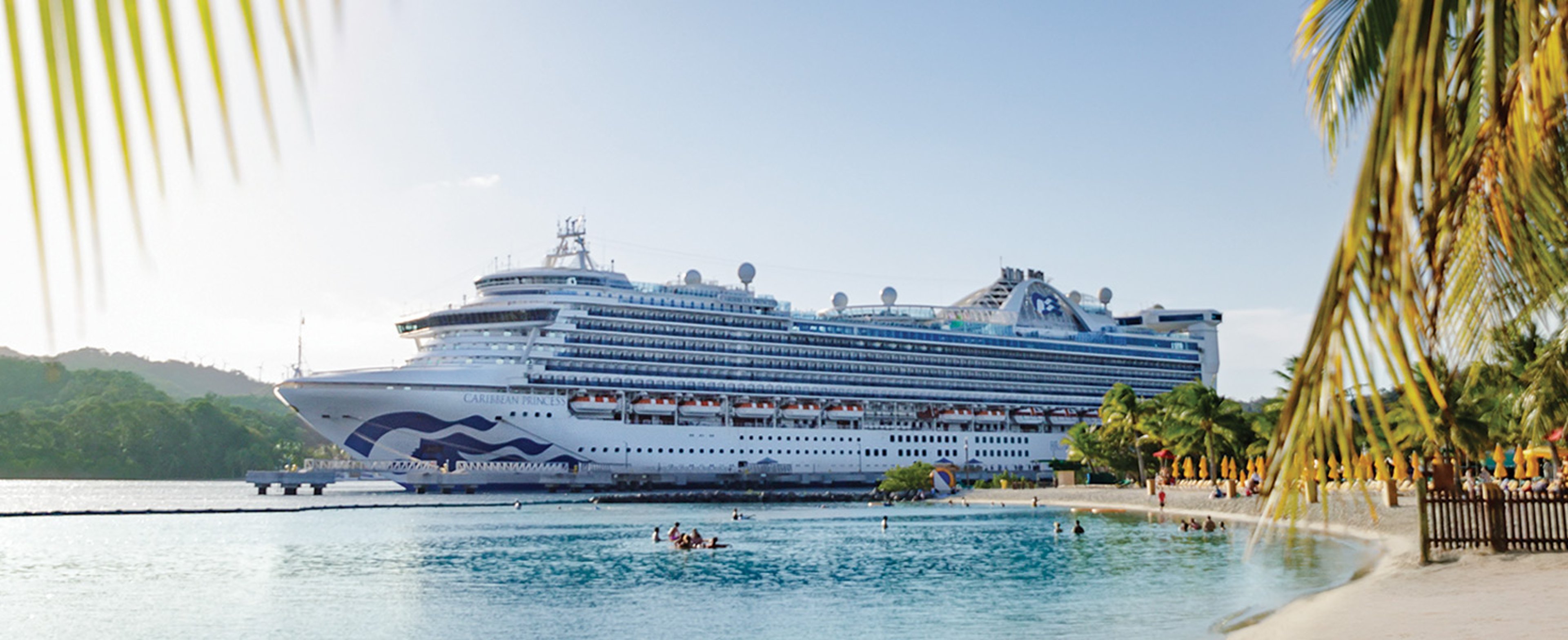 The Caribbean Princess docked in Mahogany Bay in Roatan Honduras, framed by the beach and a palm tree