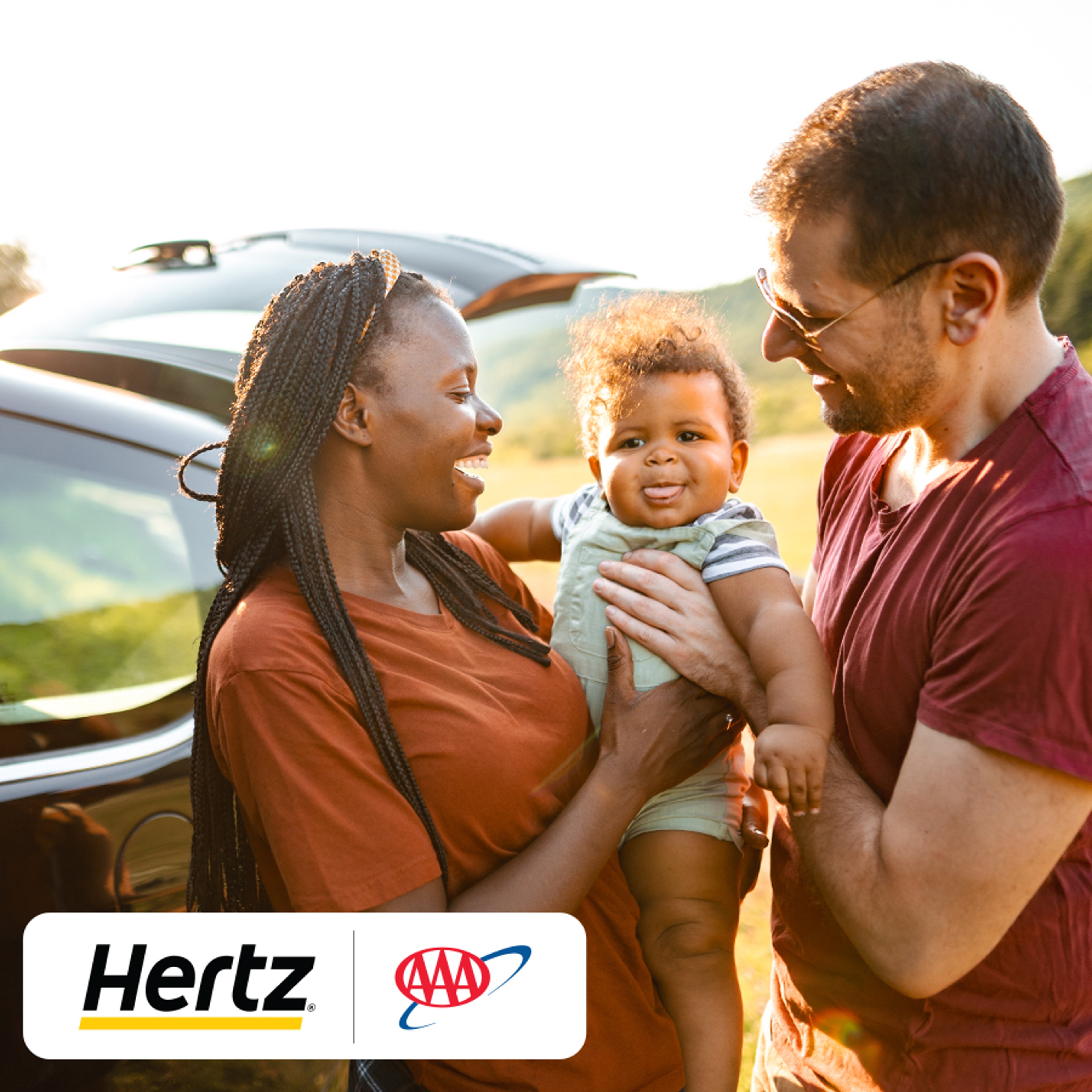 Couple holding a baby between them, standing next to their car with the trunk up.