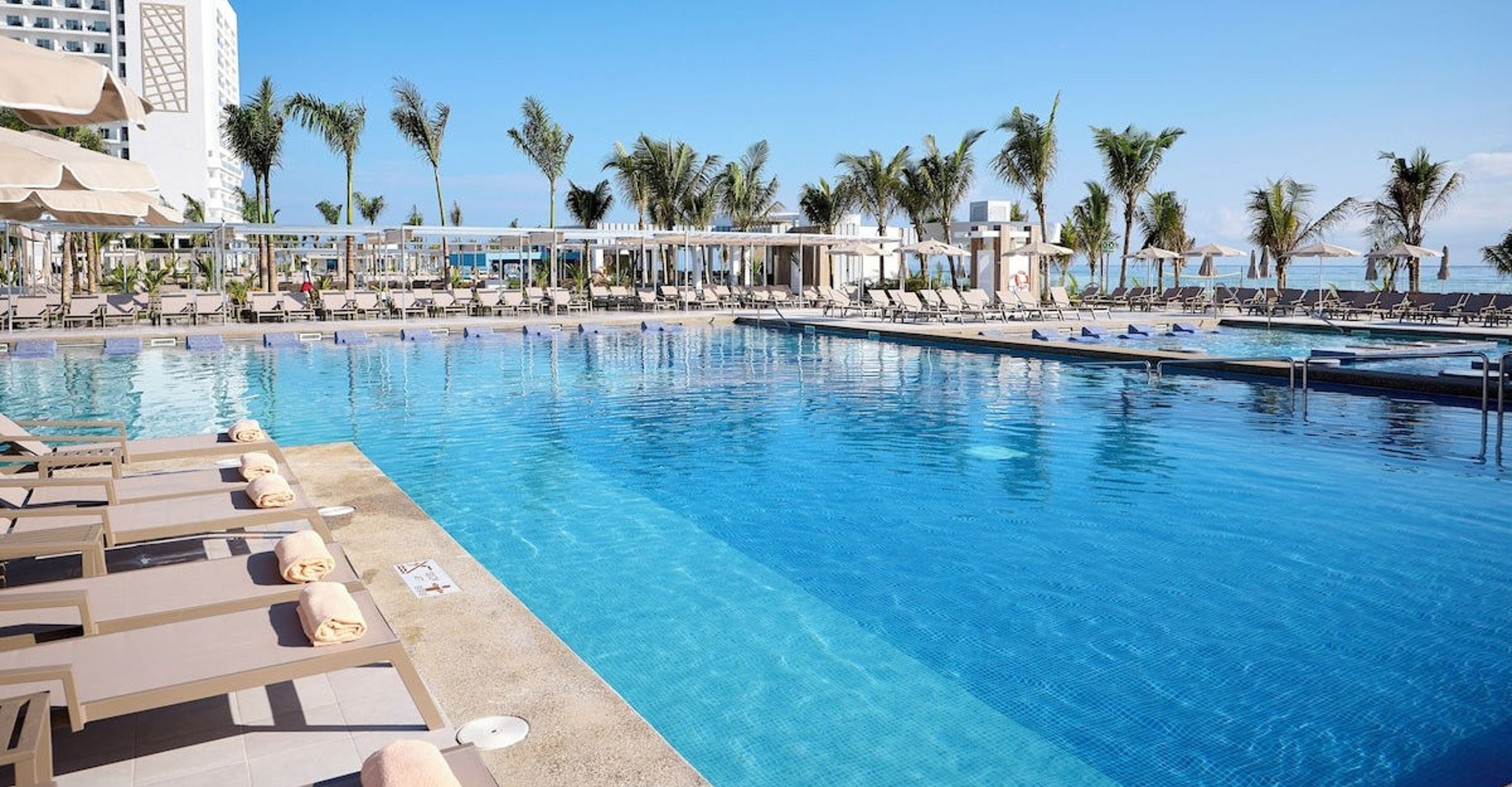 Large outdoor swimming pool at a resort with lounge chairs and a view of the ocean