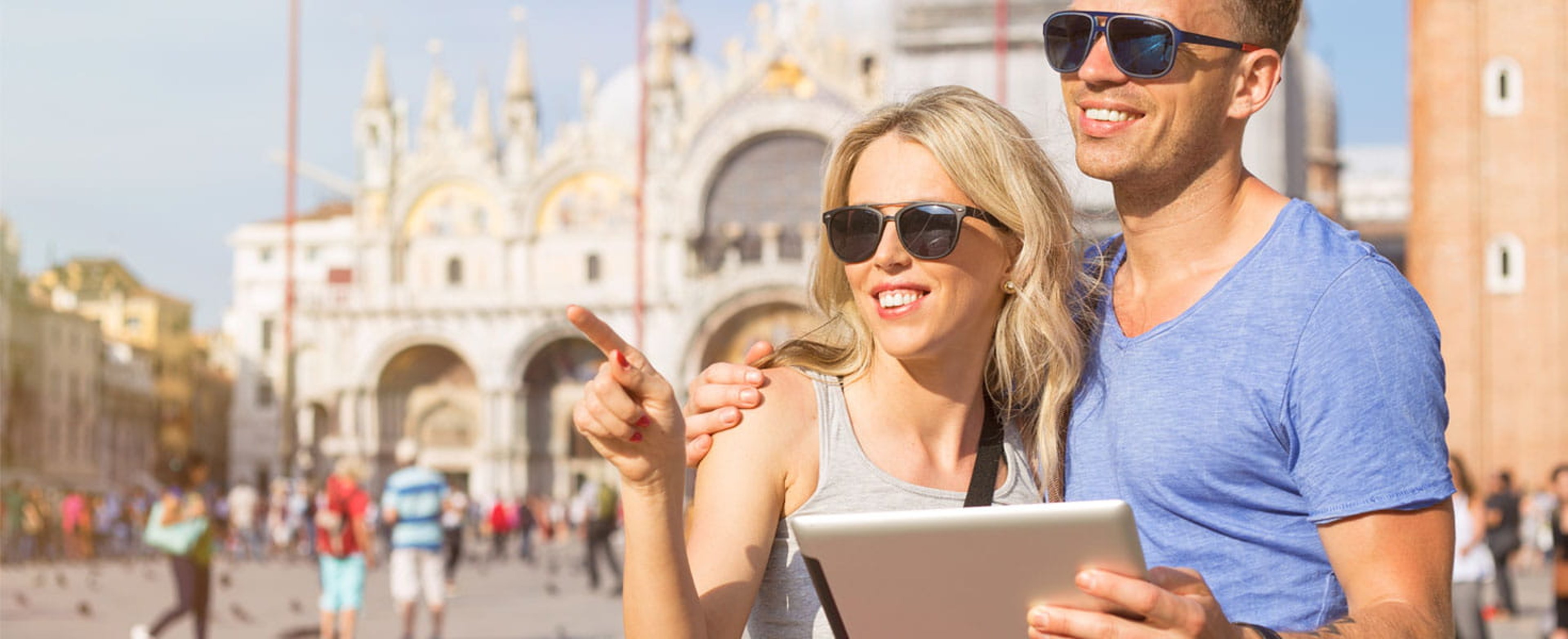 Traveling couple with sunglasses looking at tablet with ornate white and gold accented building in background
