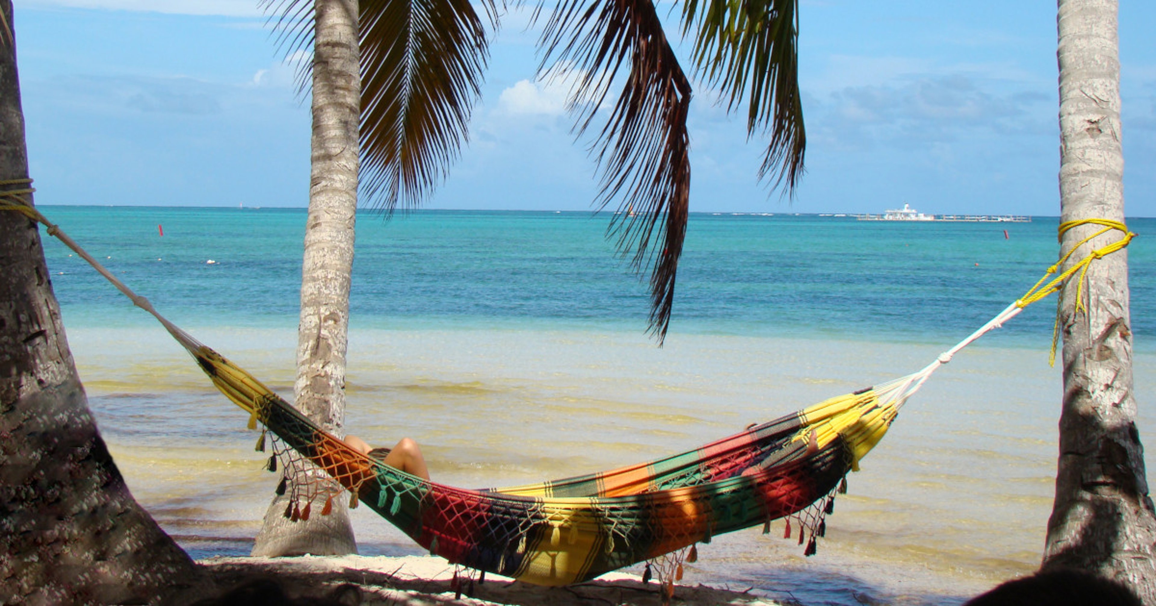 Woman in multicolor hammock on Punta Cana beach under palm trees