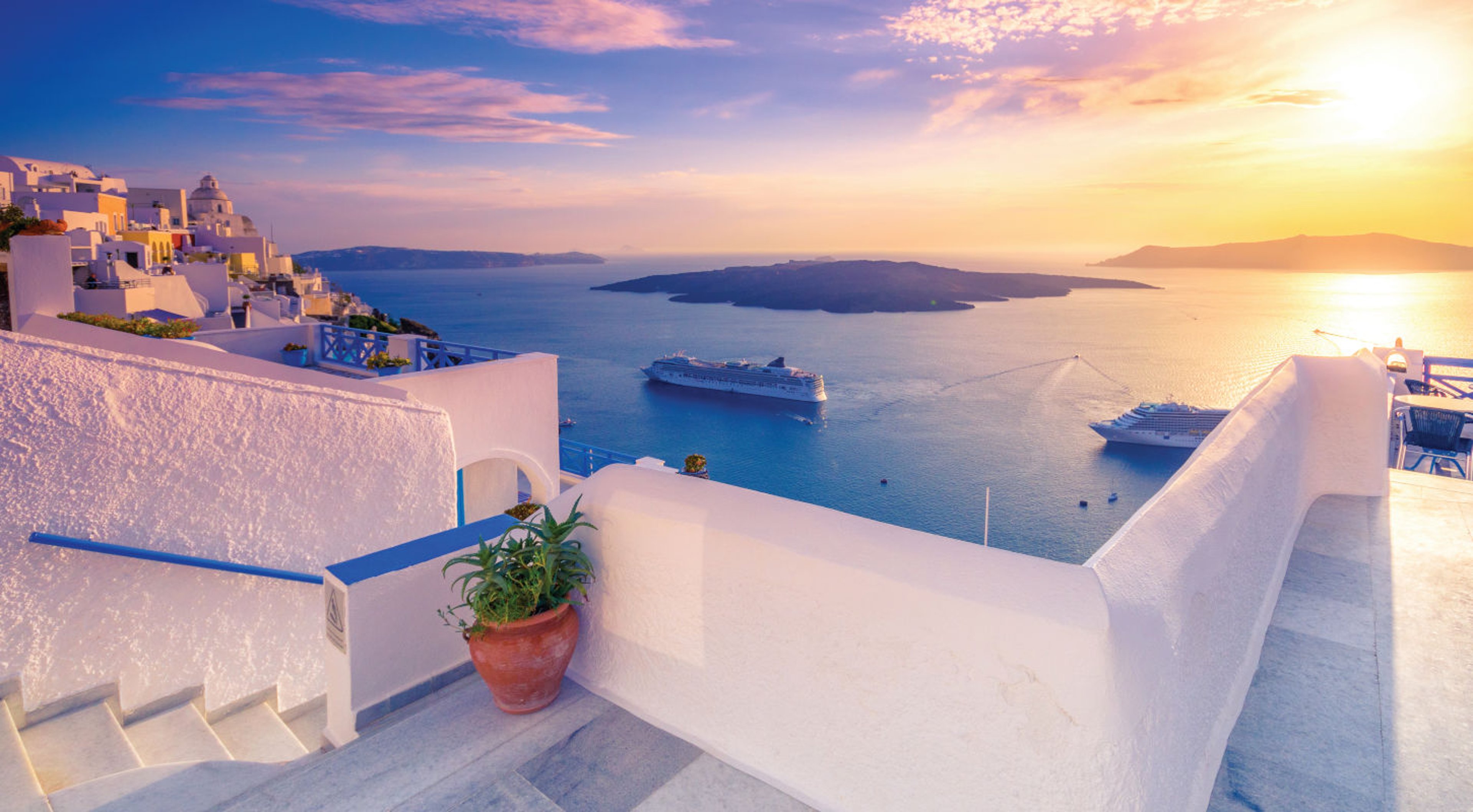 AAA Travel Set Sail Whitewashed house overlooking the caldera in Fira on the island of Santorini with cruise ships at sunset
