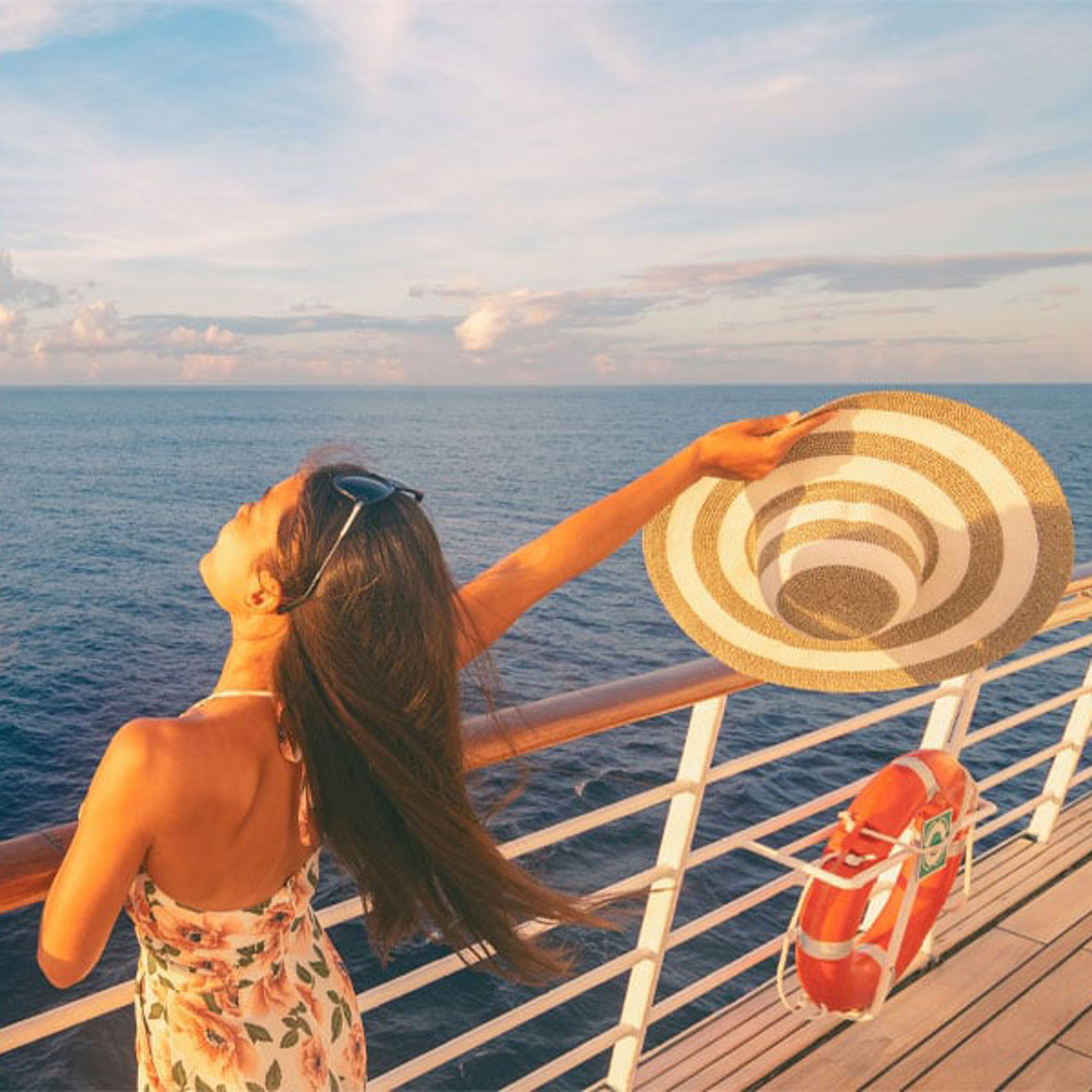 Woman in sundress with striped hat on deck of cruise ship at sunset