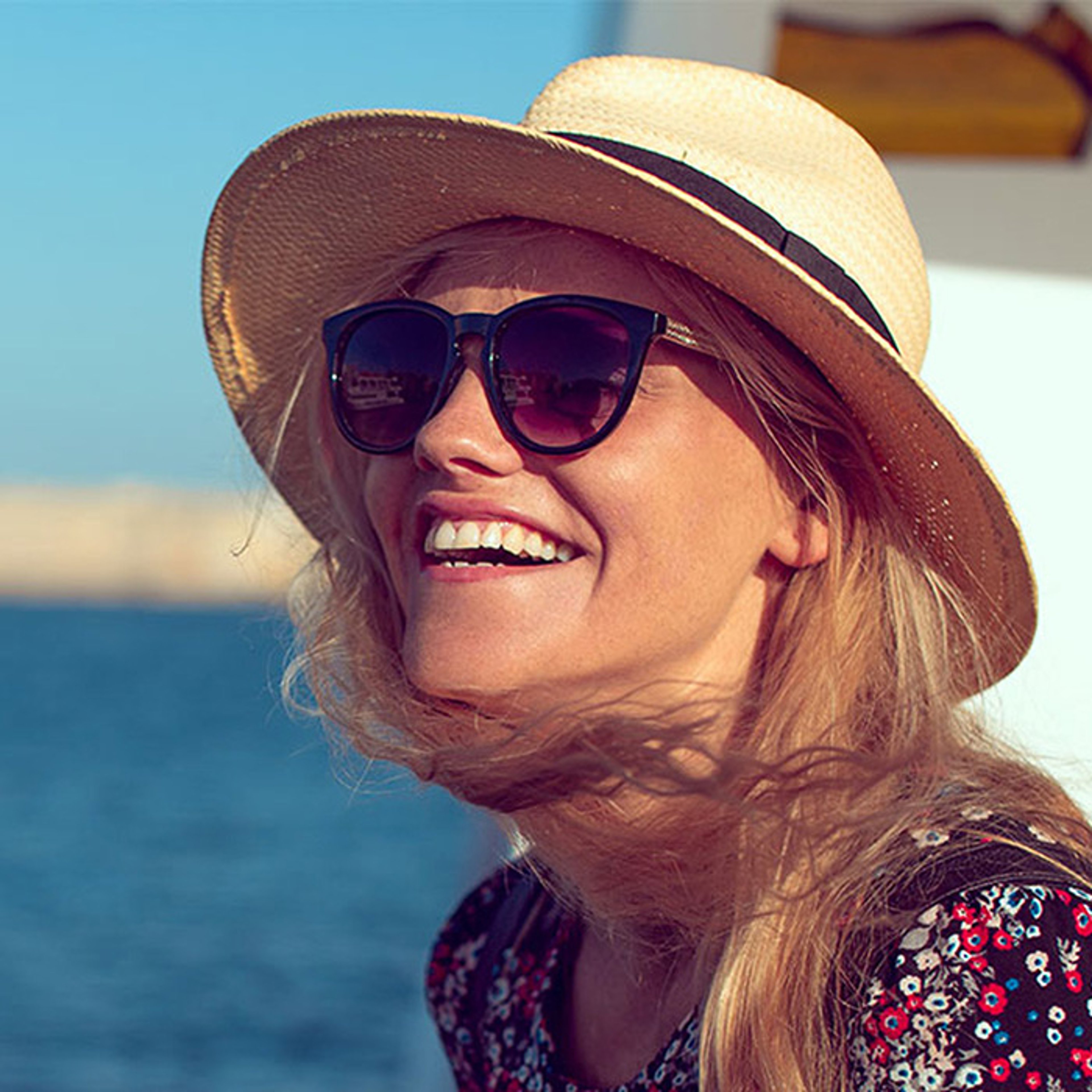 Woman with straw hat and sunglasses smiling on deck of ocean cruise