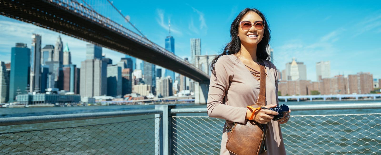 A woman posing by a bridge holding a camera