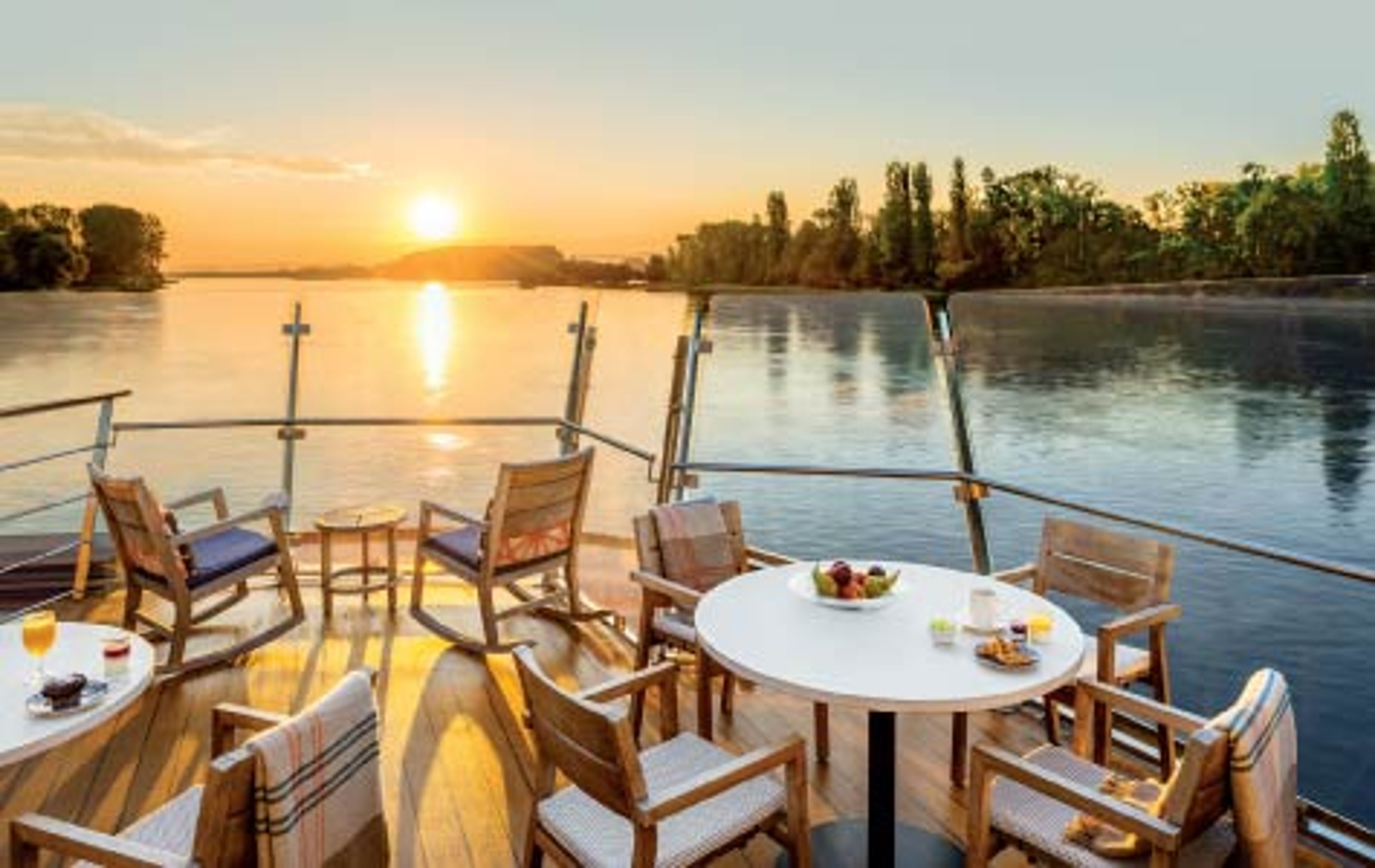 Sunrise view from a Viking river cruise ship deck with lounge chairs overlooking calm water and tree-lined shores.
