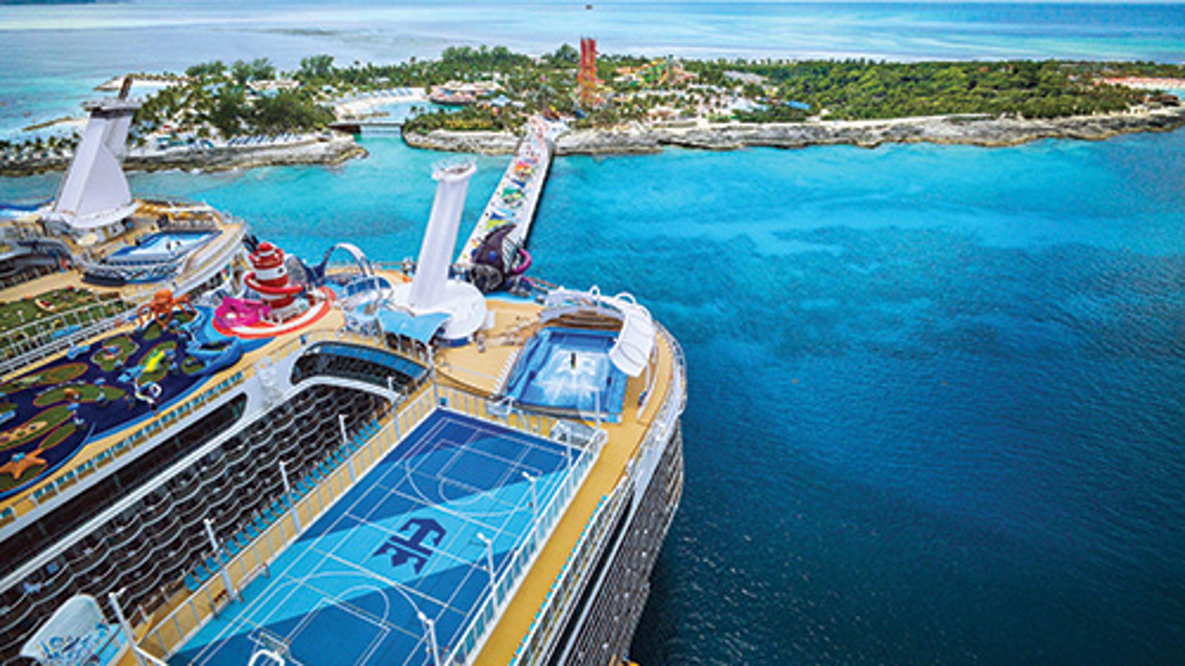 Aerial view of a Royal Caribbean cruise ship with a sports court and waterslides, near a tropical island and turquoise ocean.