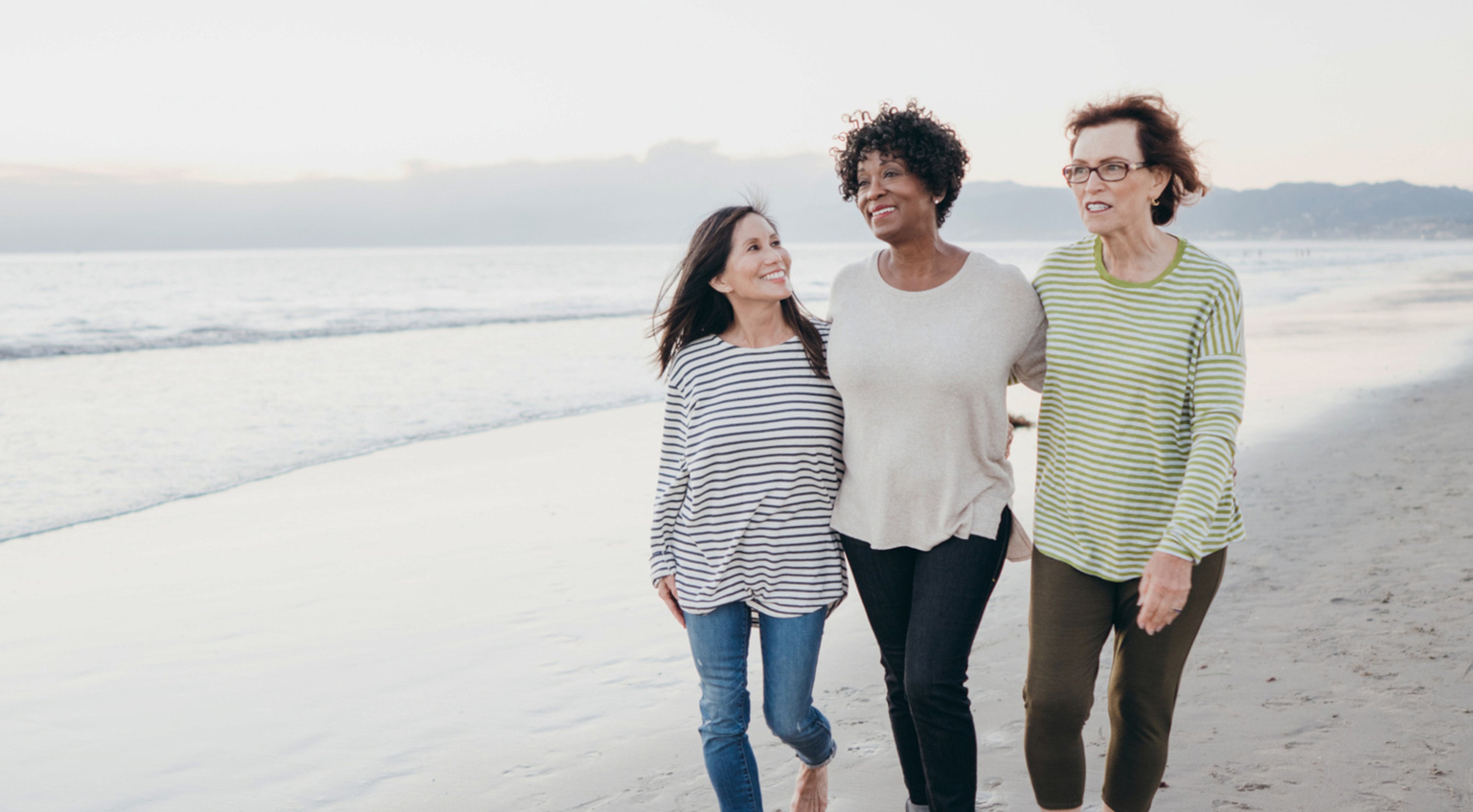 Three older women walking on the beach at sunrise