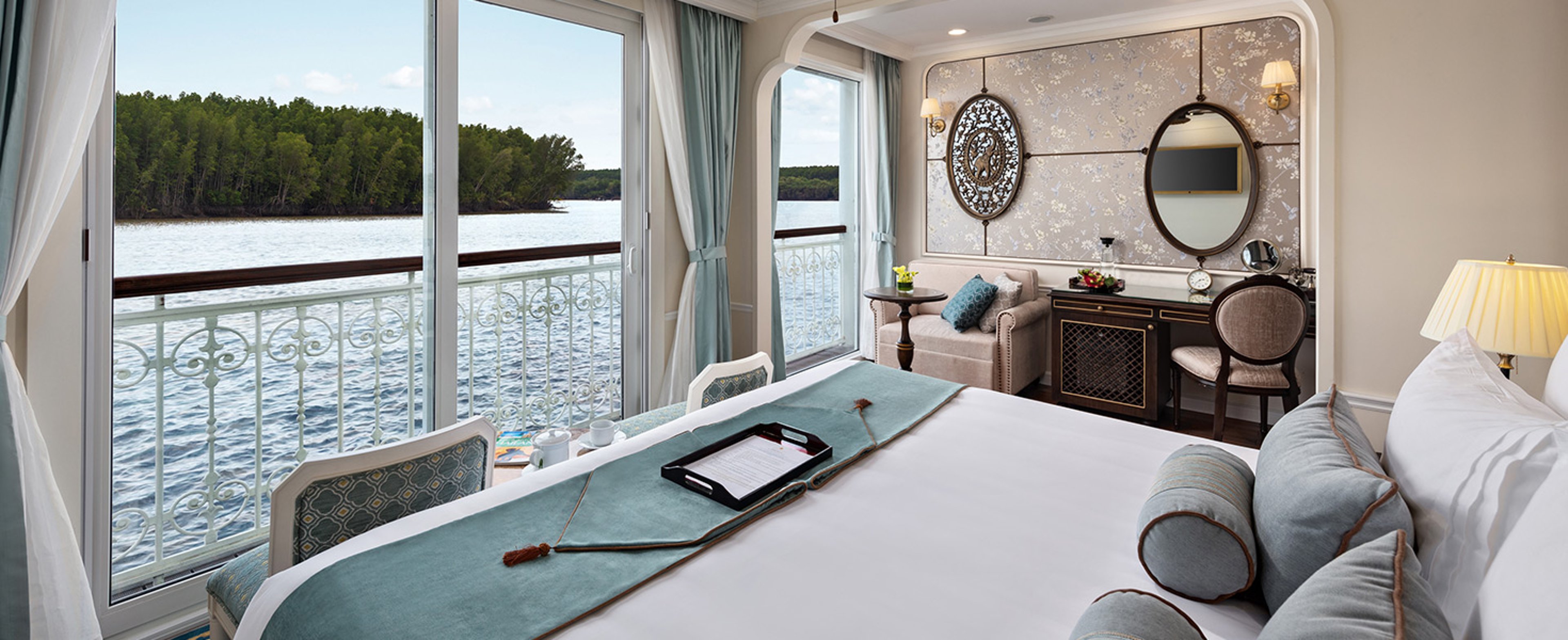 Balcony stateroom aboard Uniworld's Mekong Jewel with view of Mekong river visible through the balcony doors.