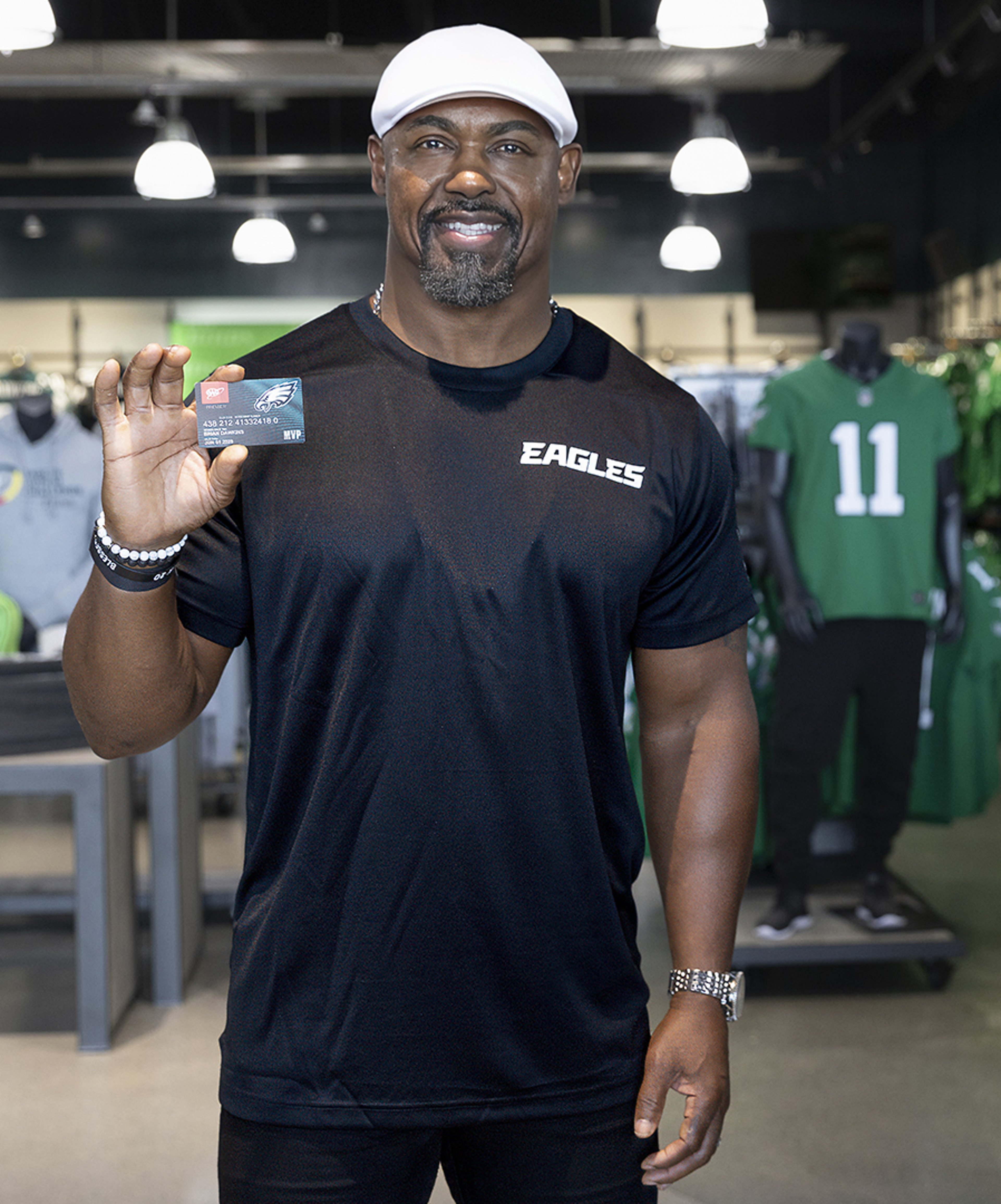 Philadelphia Eagles legend Brian Dawkins holding a AAA Eagles MVP card while standing in Eagles Pro Shop