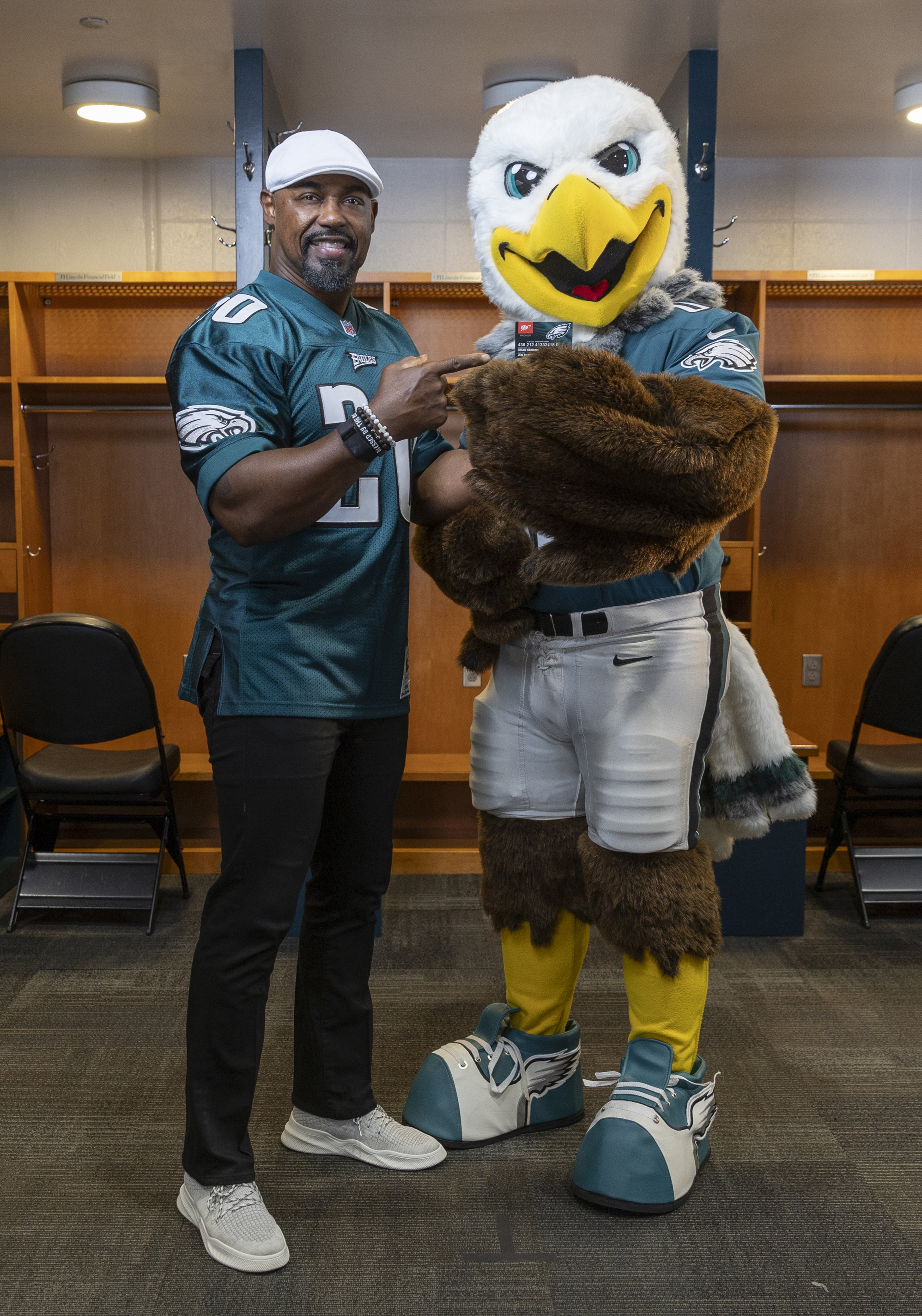 Philadelphia Eagles legend Brian Dawkins pointing at Eagles mascot Swoop holding a AAA Eagles MVP card while standing in Eagles locker room