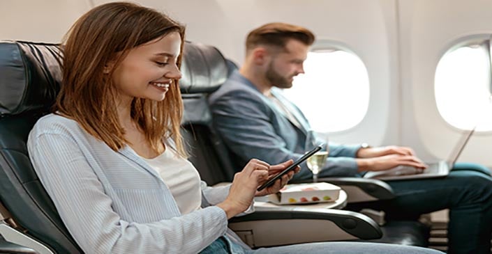Airplane cabin with two passengers, a woman using a smartphone and a man using a laptop.