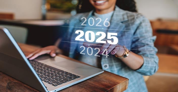 A woman in a blazer points at a digital display of the years 2024, 2025, and 2026 with 2025 highlighted.