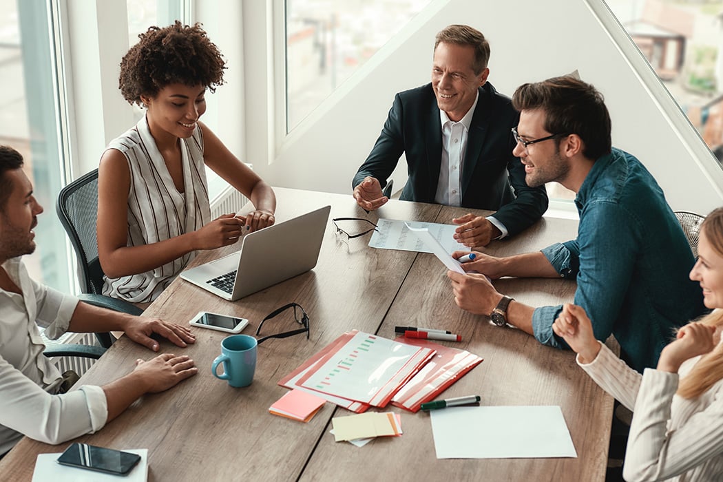 Diverse group of happy business professionals chatting in conference room with notes and coffee on the table
