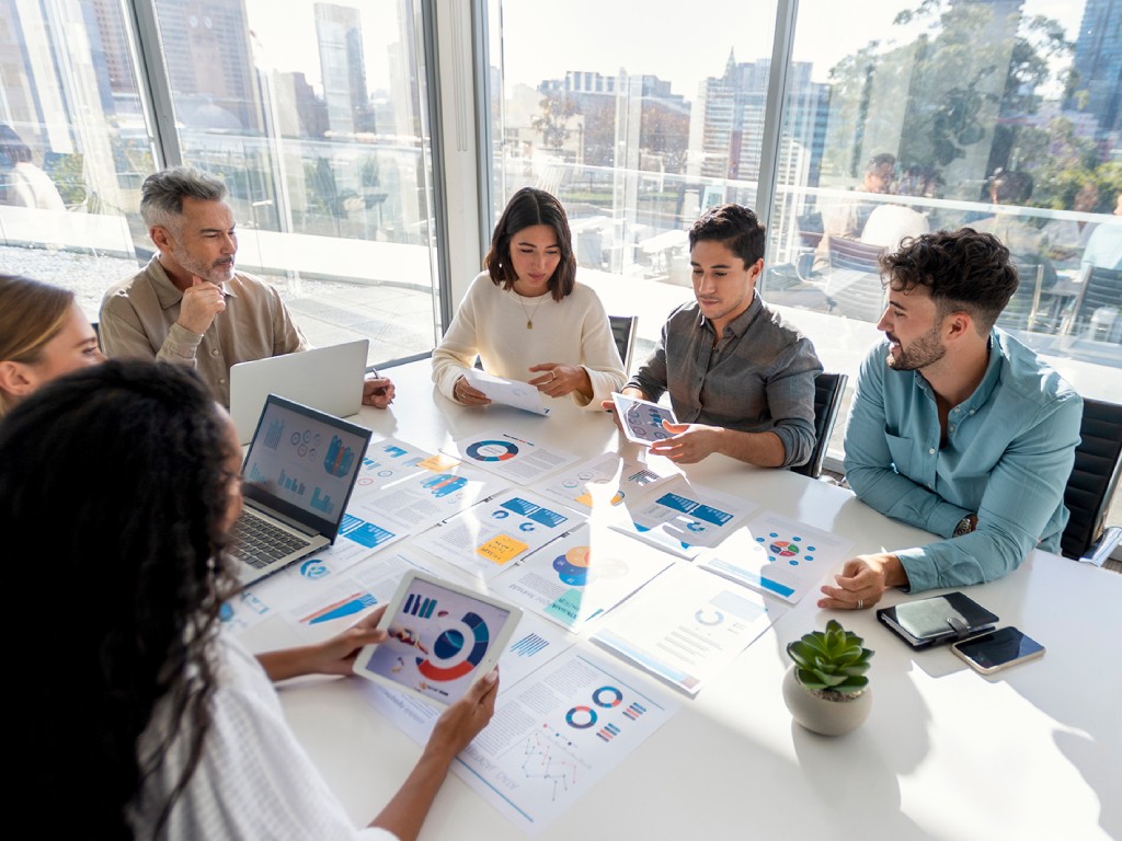 A team of business professionals discusses charts and graphs in a bright conference room.