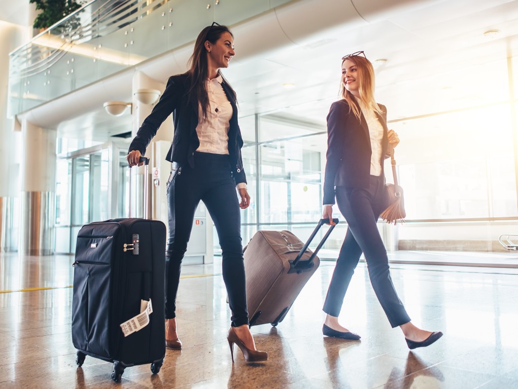 Two business women walking through the airport with rolling luggage