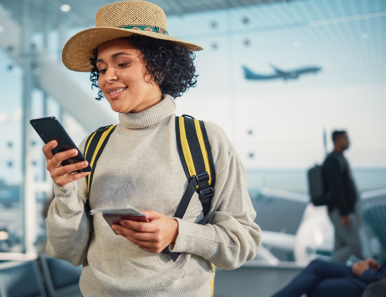 Woman looking at smartphone in airport terminal with plane in background