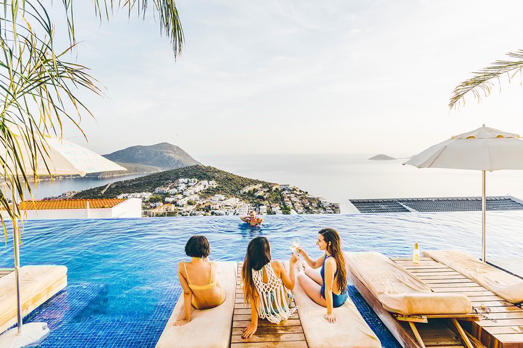 Three women friends in bathing suits lounging by infinity pool at island resort 