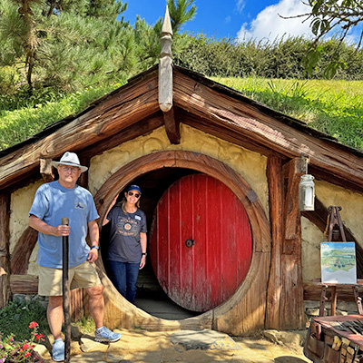 Martin Travel advisor Judy Miron and her husband standing in front of iconic red door on Hobbiton movie set, Auckland, New Zealand