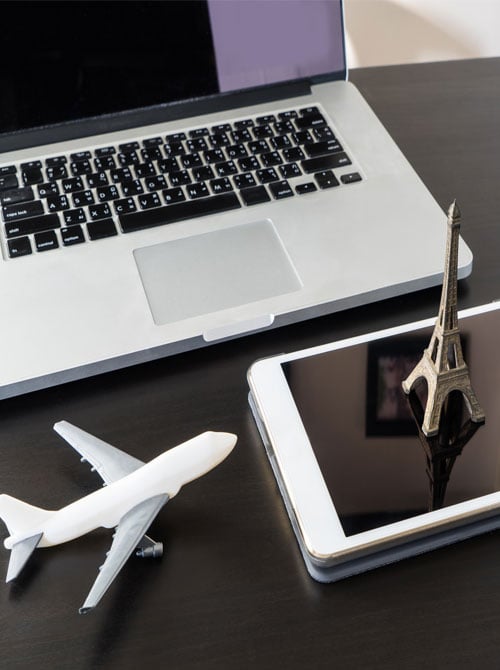 Laptop with model airplane and Eiffel tower model sitting on tablet